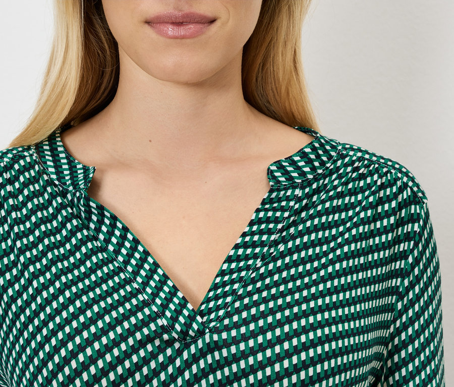 Zbliżenie kobiety o blond włosach, ubranej w zielono-białą bluzkę w kratę.