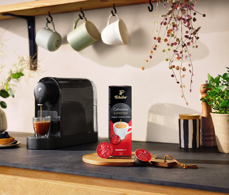 Ekspres do kawy nalewa kawę do szklanki obok opakowania Cafissimo Espresso elegant.