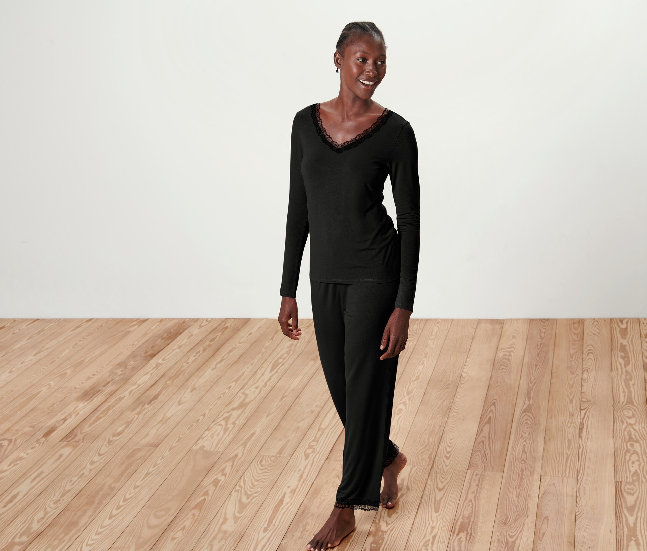 Kobieta w czarnej piżamie z koronką pozuje na drewnianej podłodze.
