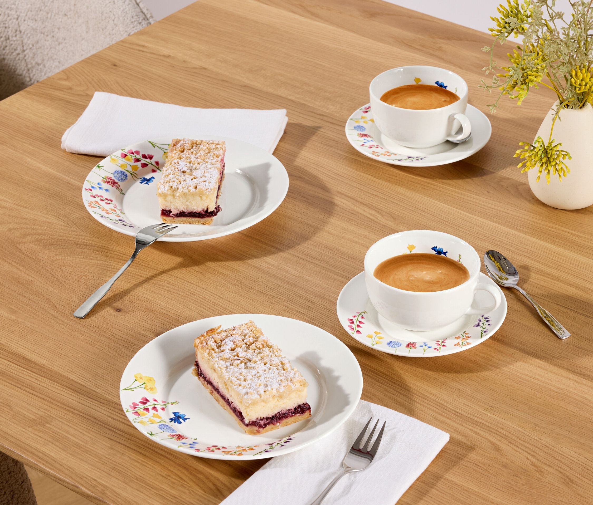 Dwa kawałki ciasta i dwie filiżanki kawy na drewnianym stole.