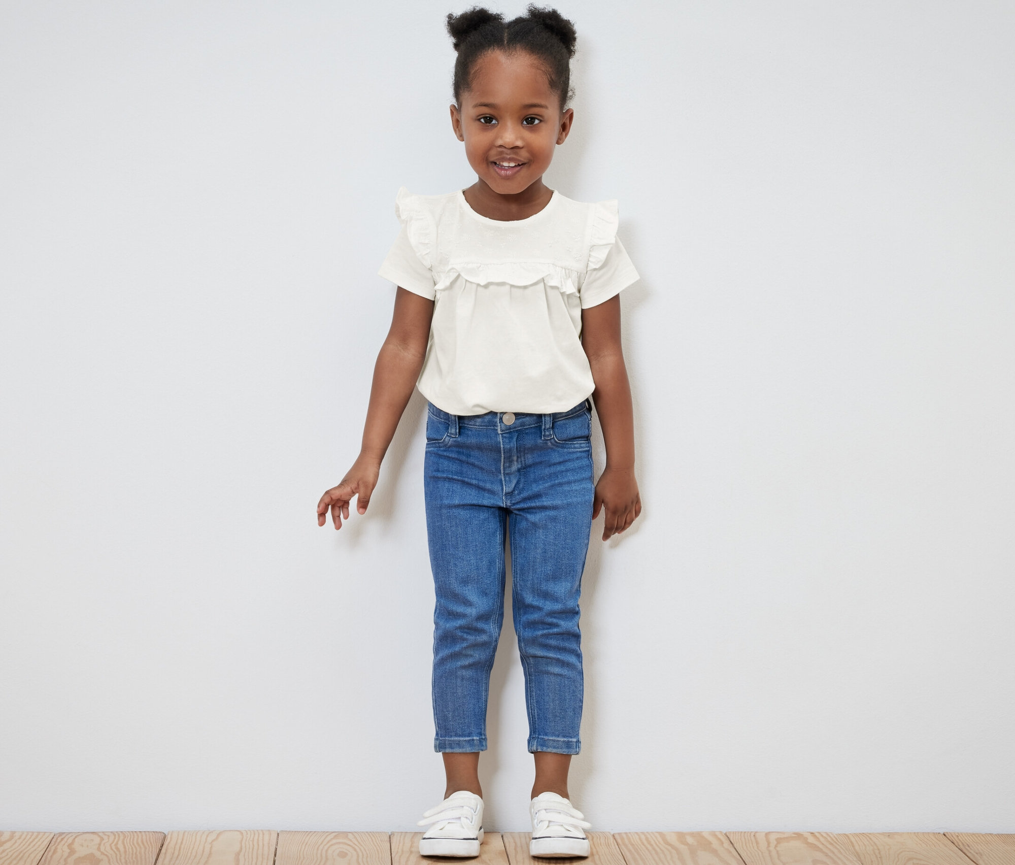 Uśmiechnięta dziewczynka pozuje w jasnej koszulce i niebieskich dżinsach.