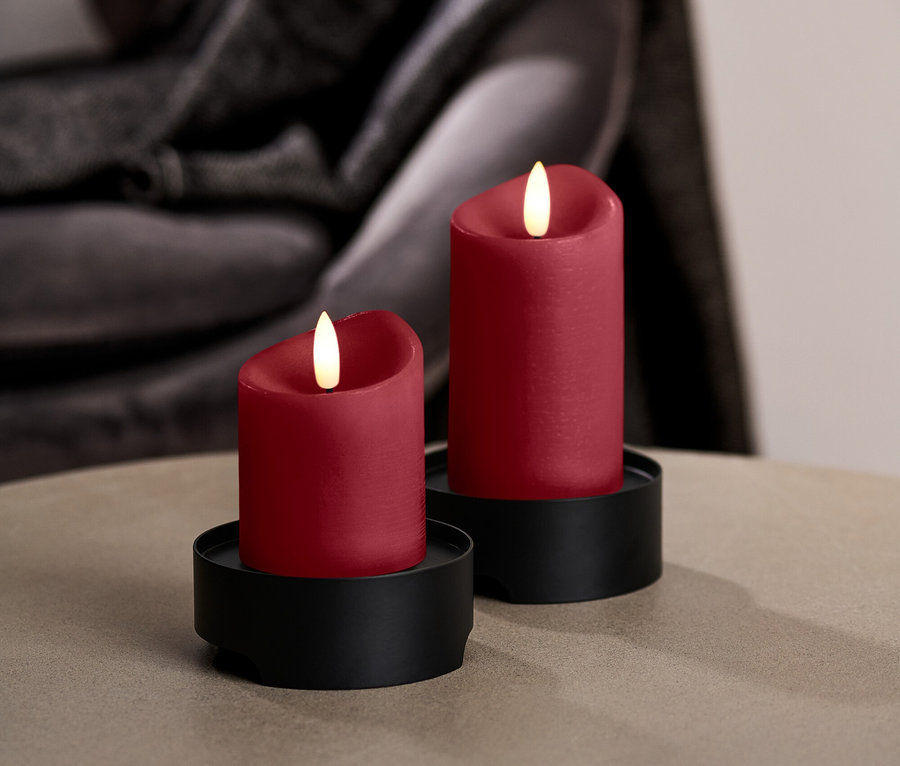 Dwie czerwone świece LED na czarnych podstawkach stoją na okrągłym stole.