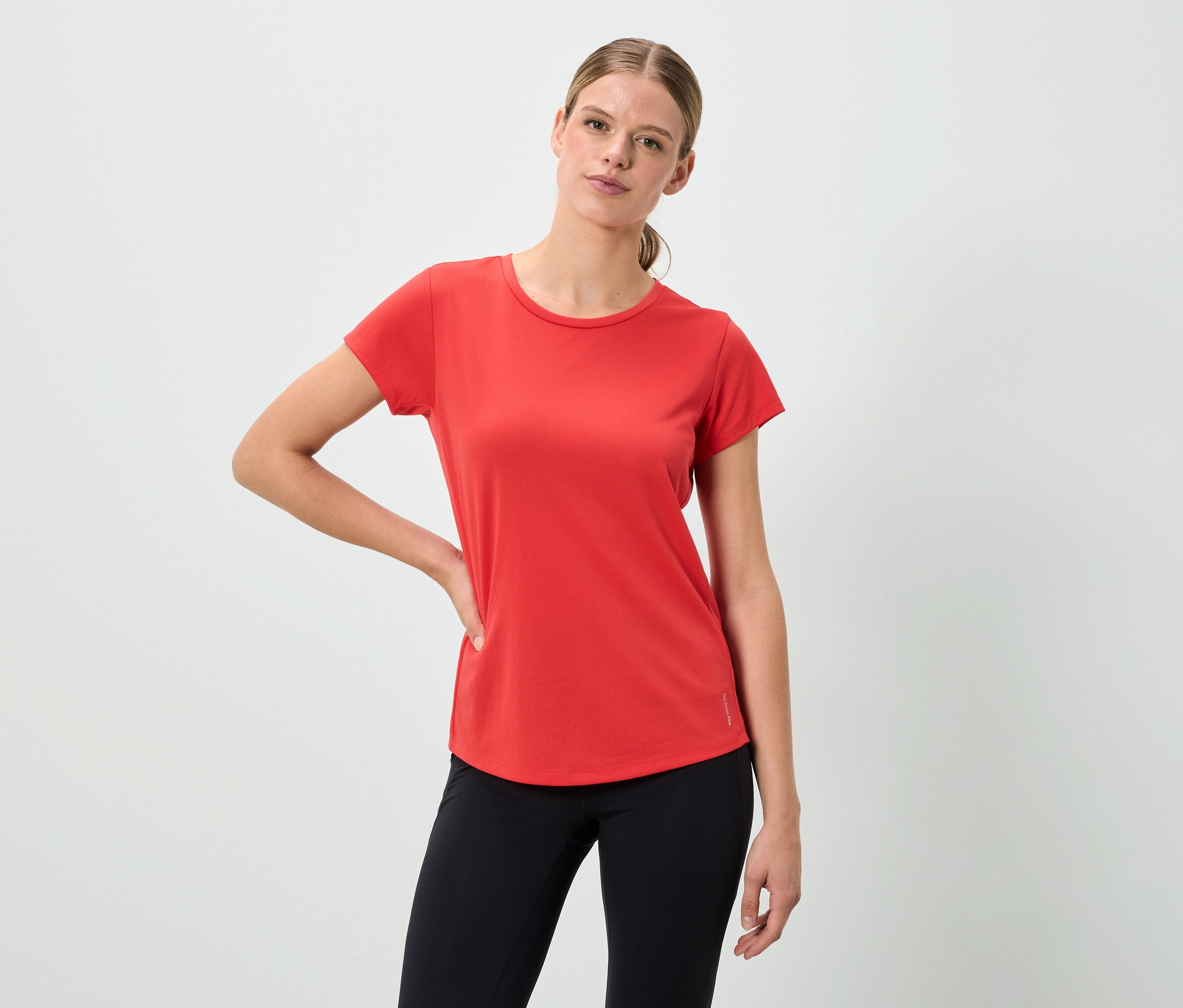 Kobieta pozuje w czerwonym T-shircie i czarnych legginsach.