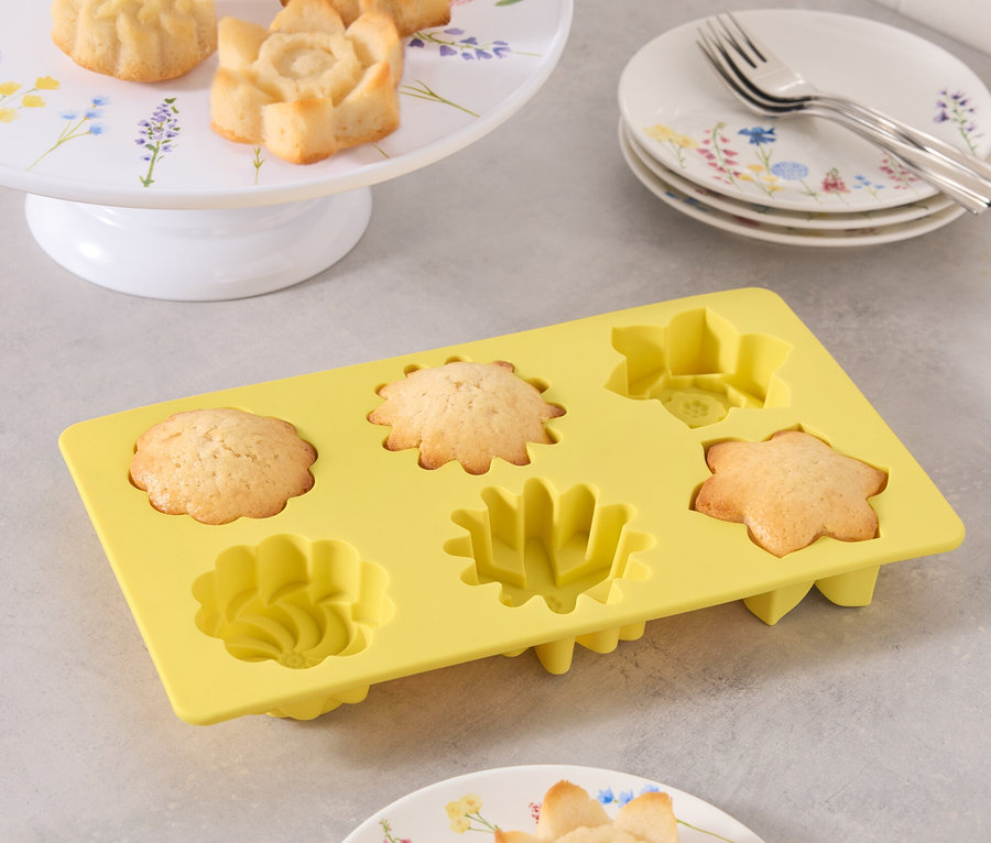 Foremki do ciast w kształcie kwiatów na talerzu i w żółtej formie silikonowej.