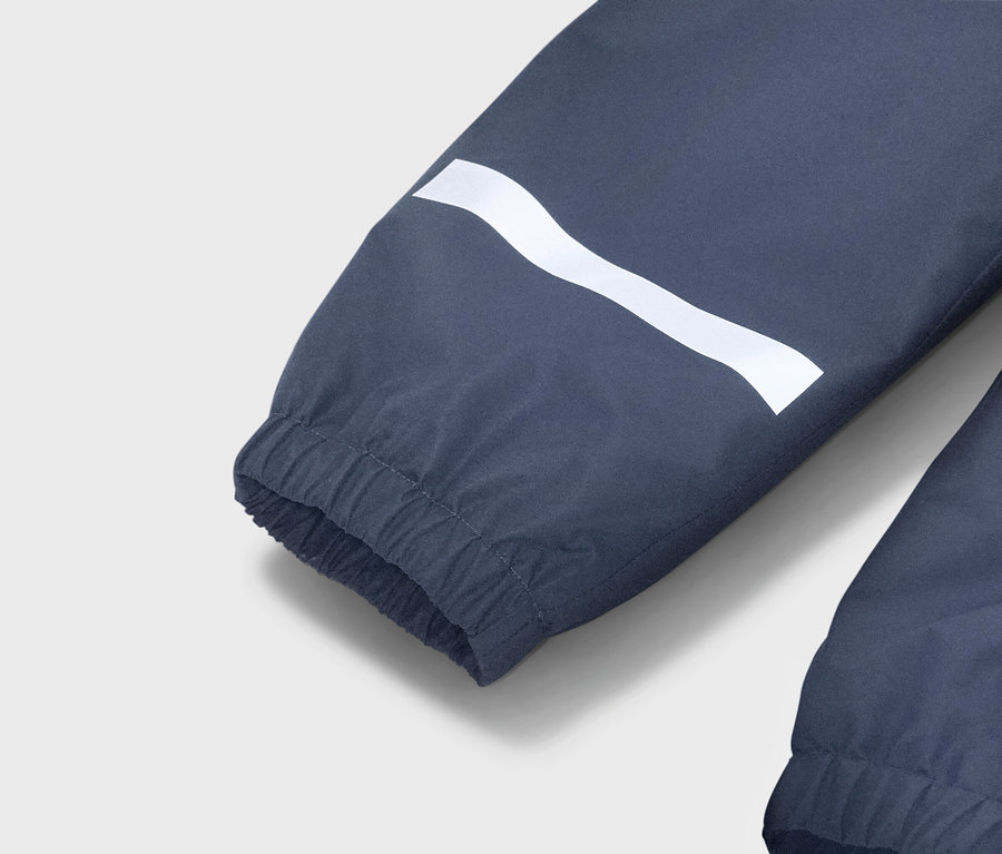 Zbliżenie na niebieski rękaw kurtki z białym, falistym paskiem i elastycznym mankietem.