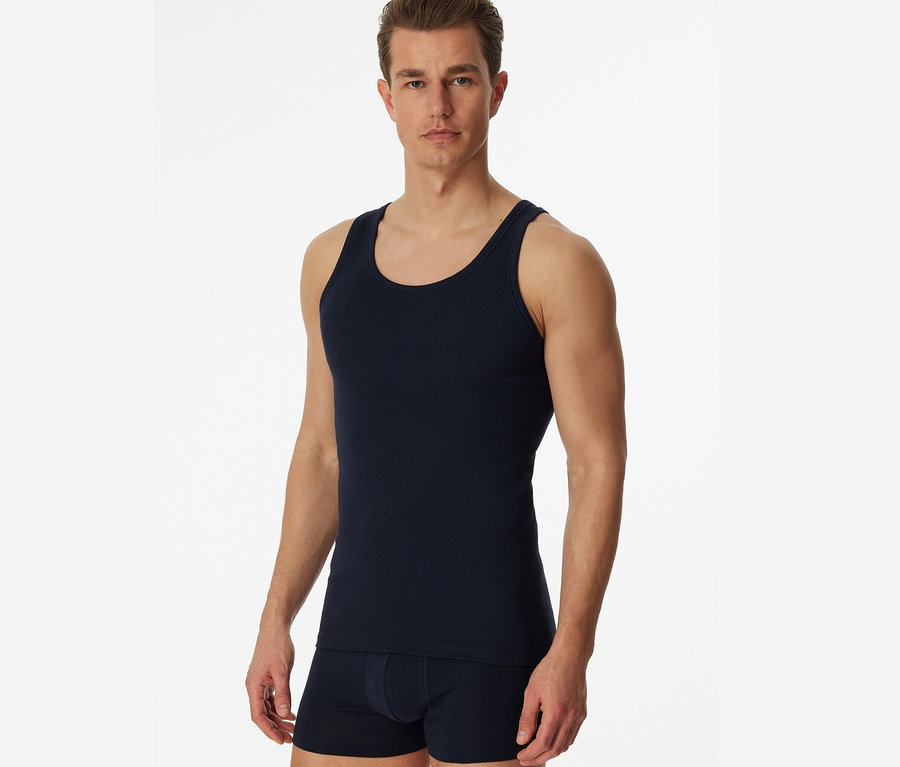 Mężczyzna pozuje na białym tle w granatowej podkoszulce trykotowej SCHIESSER, 2 sztuki.