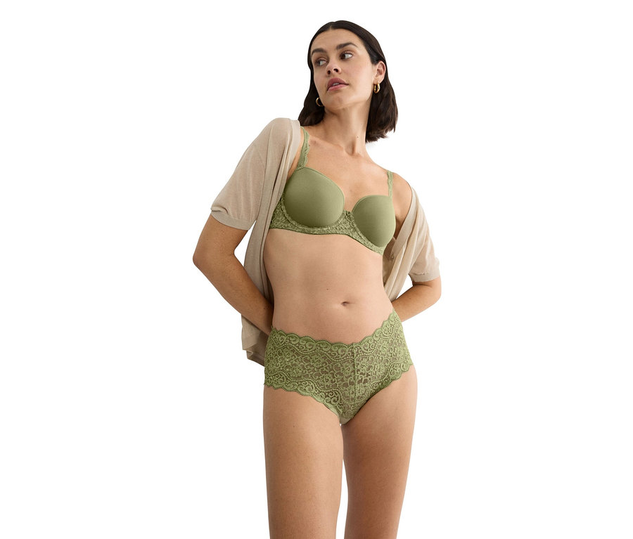Kobieta ma na sobie zielony biustonosz z koronkowym wykończeniem i pasujące koronkowe majtki oraz beżowy kardigan.