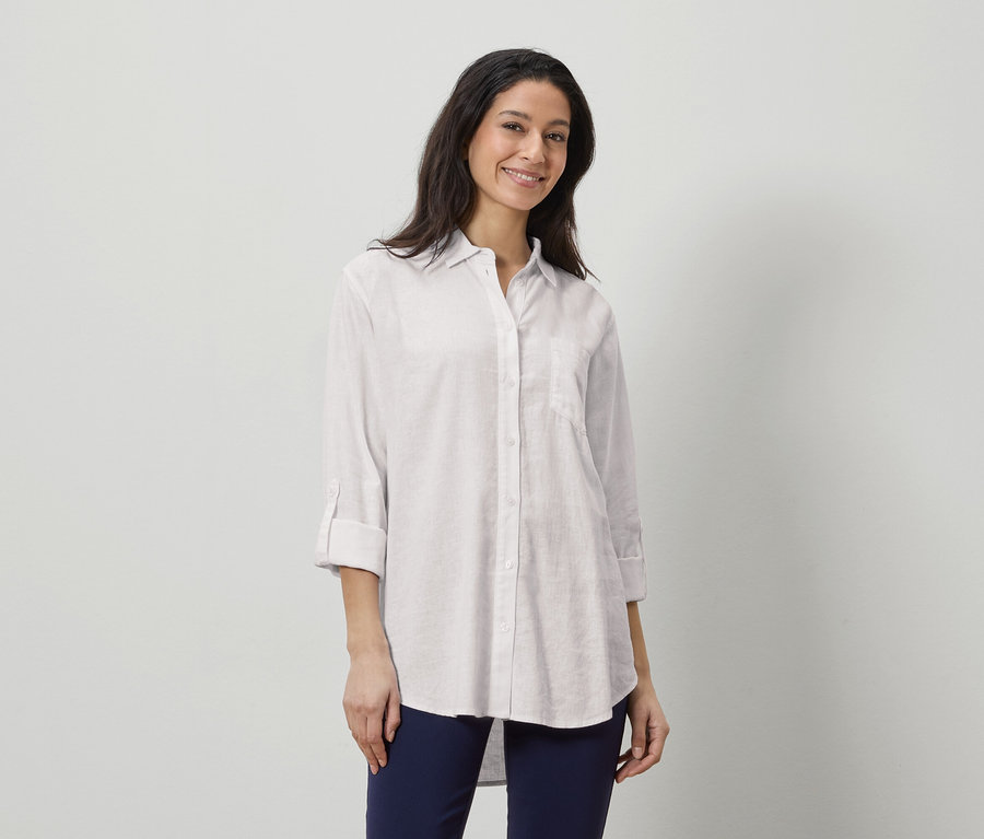 Kobieta ma na sobie białą lnianą koszulę i granatowe spodnie.
