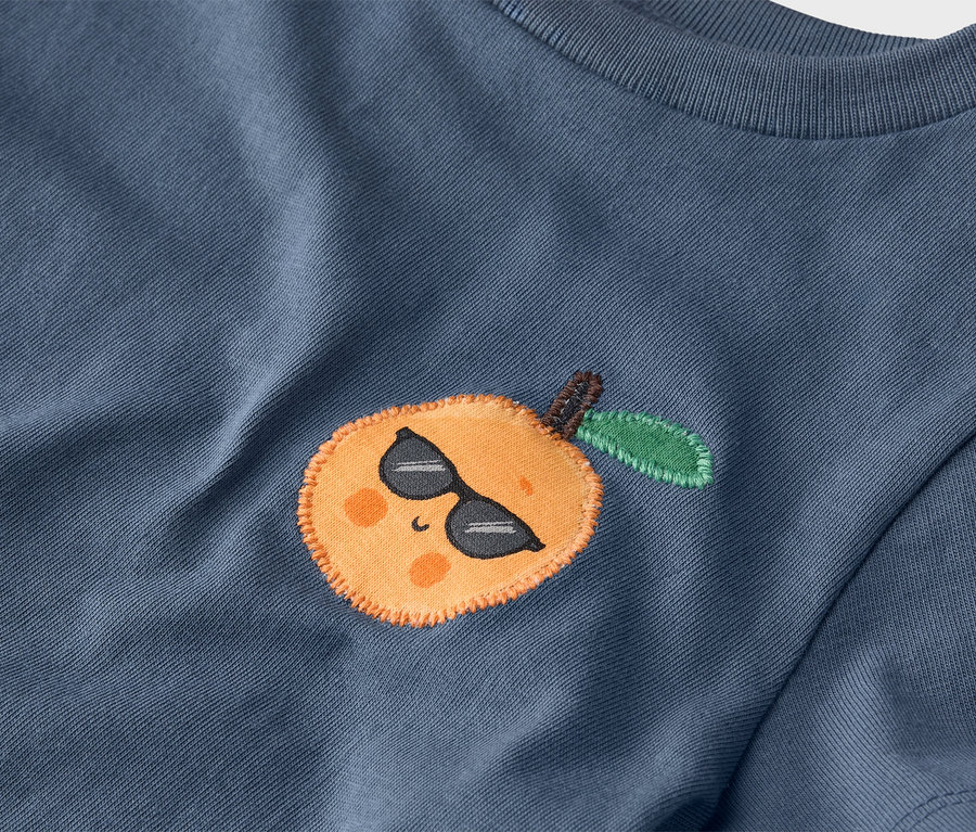 Zbliżenie niebieskiej koszulki z naszytą mandarynką w okularach przeciwsłonecznych.