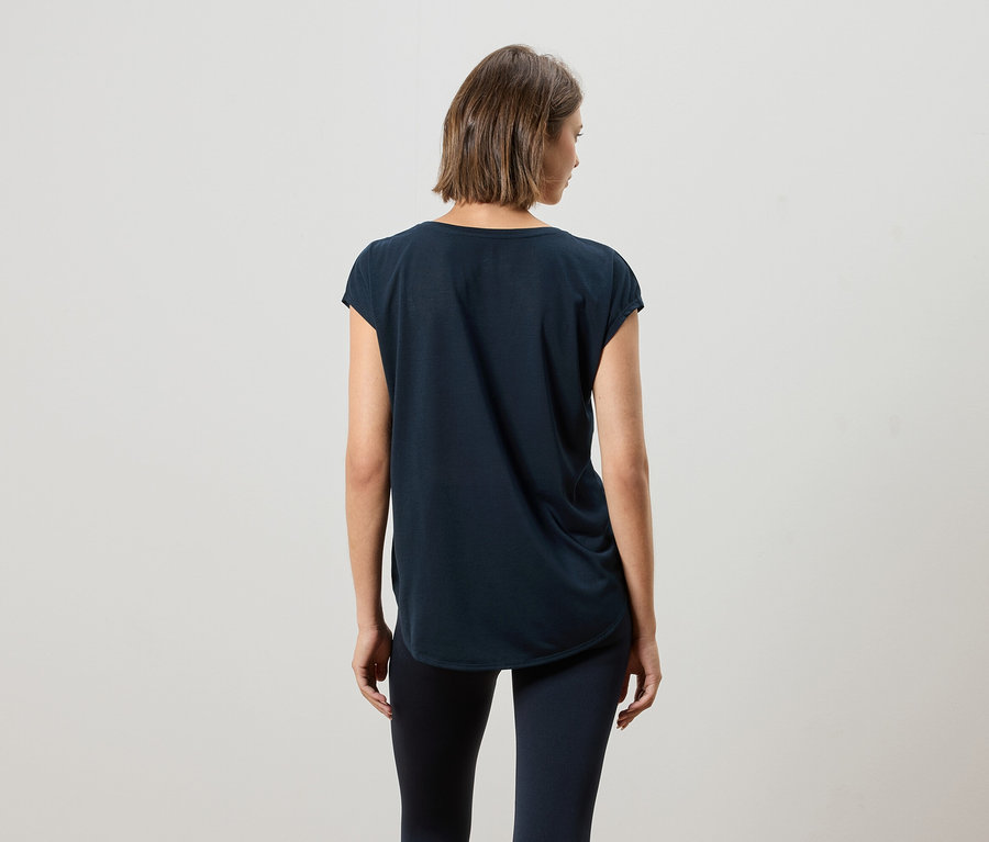 Widok z tyłu kobiety z krótkimi brązowymi włosami, ubranej w ciemnoniebieski T-shirt i legginsy.