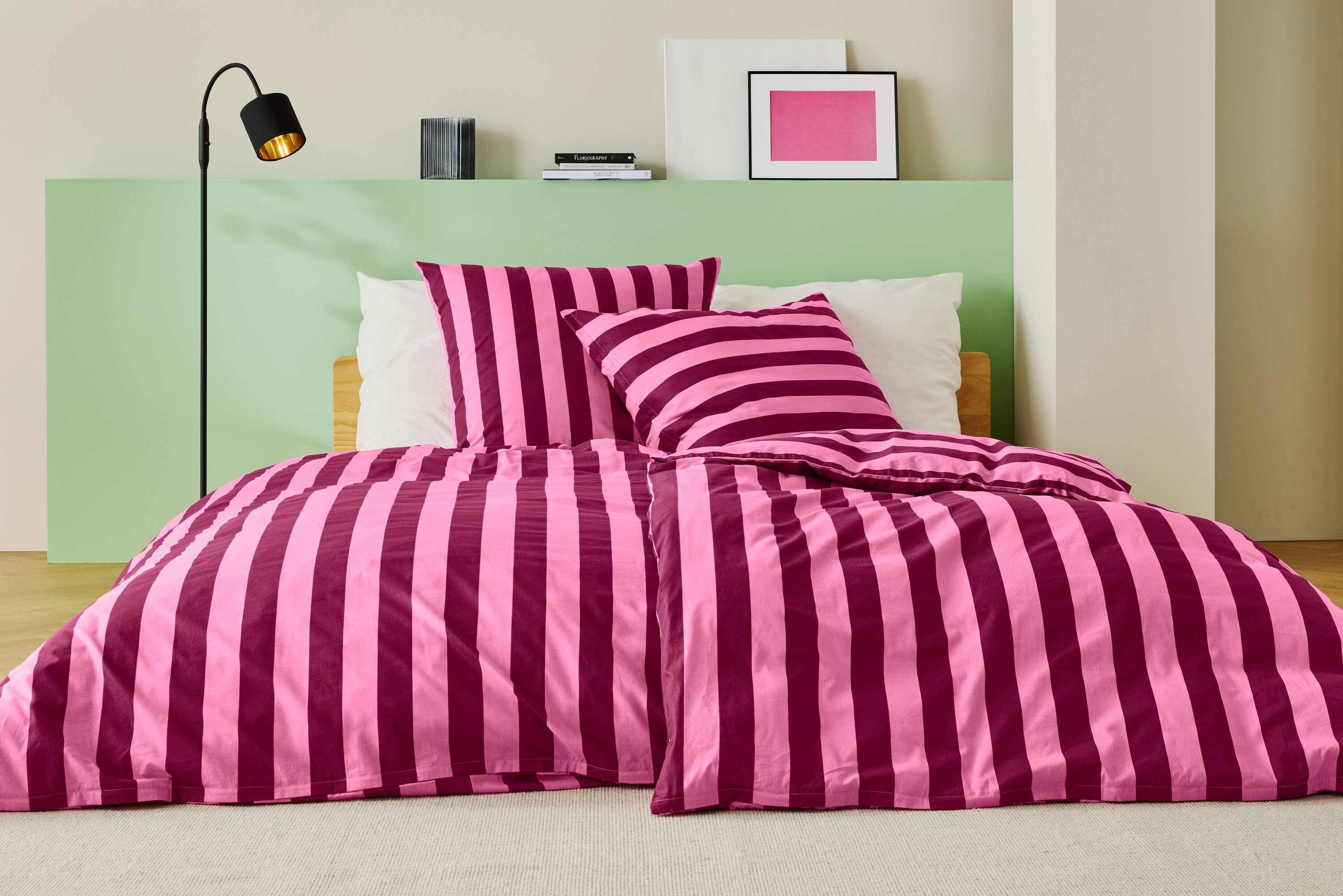 Łóżko z różowo-bordową pościelą w paski, dwiema poduszkami i lampą podłogową.