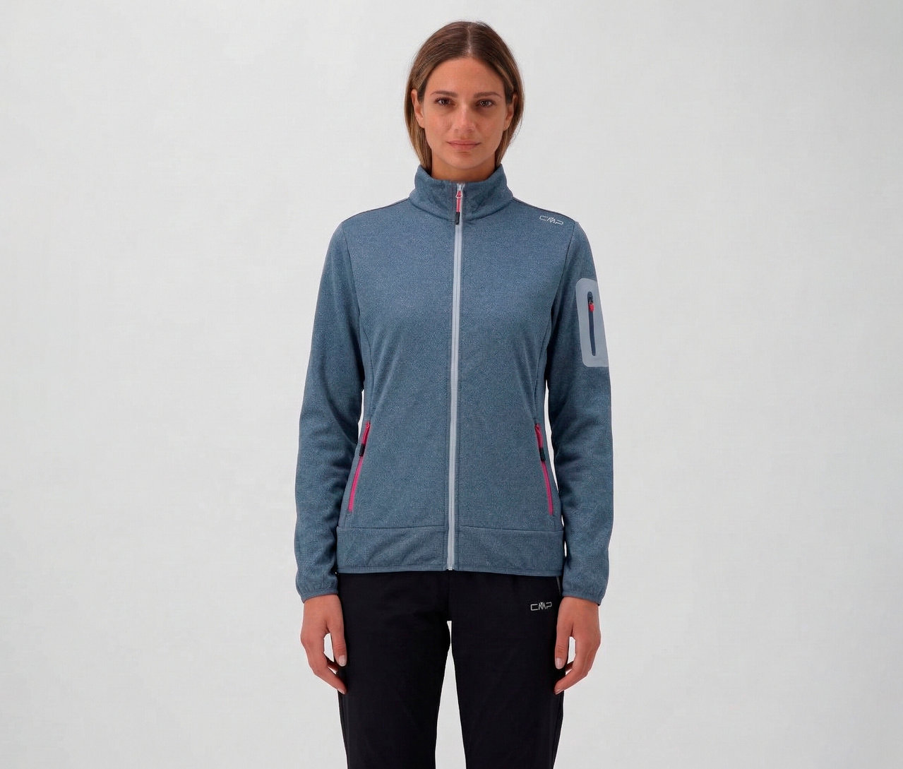 Kobieta ma na sobie rozpinaną bluzę CMP w kolorze niebieskim z zamkiem błyskawicznym i czarne spodnie na neutralnym tle.