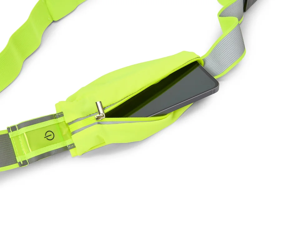 Neonowożółta saszetka biodrowa z zamkiem błyskawicznym, w której znajduje się smartfon. Na odblaskowym pasku widoczny jest symbol włącznika.