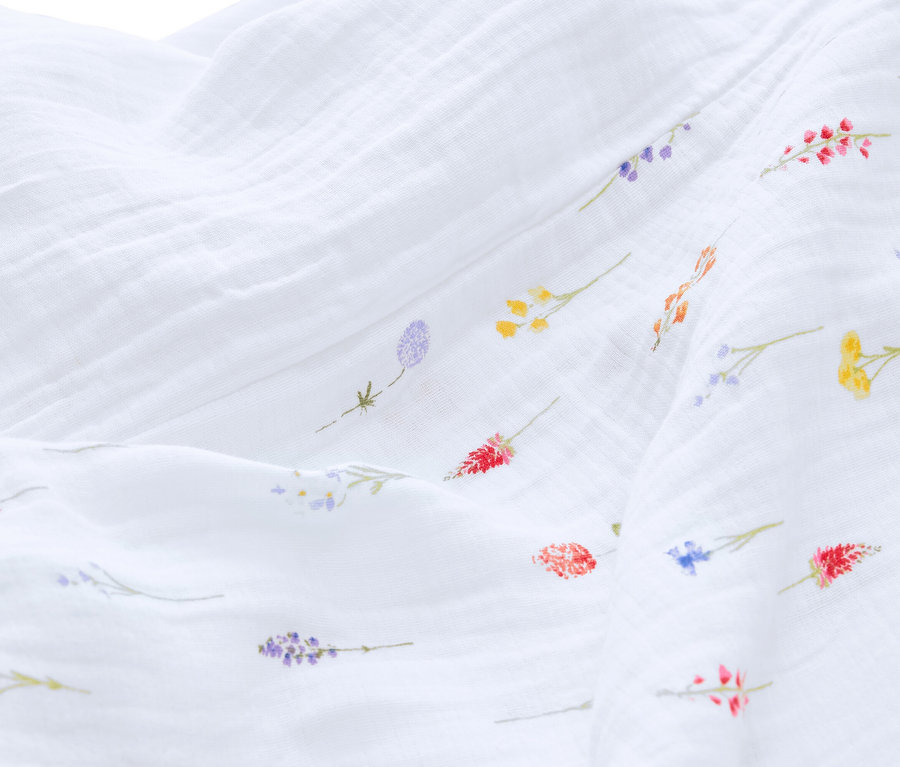 Zbliżenie białej tkaniny muślinowej z drobnymi, kolorowymi kwiatowymi wzorami.