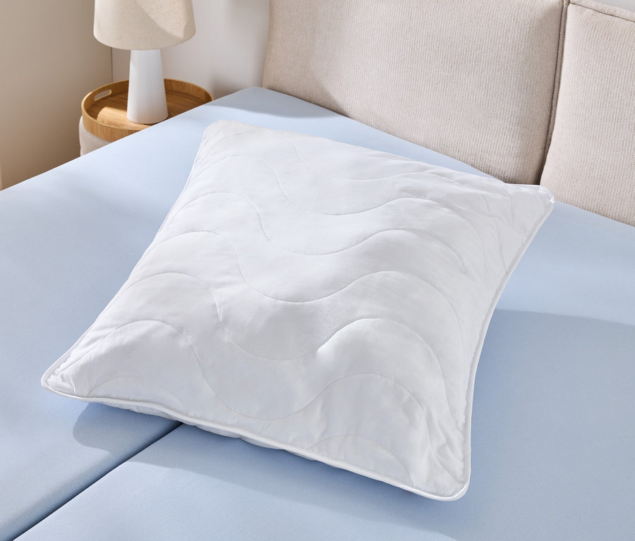 Pojedyncza biała poduszka odporna na pranie w wysokiej temperaturze (ok. 90 x 70) leży na jasnoniebieskim prześcieradle.