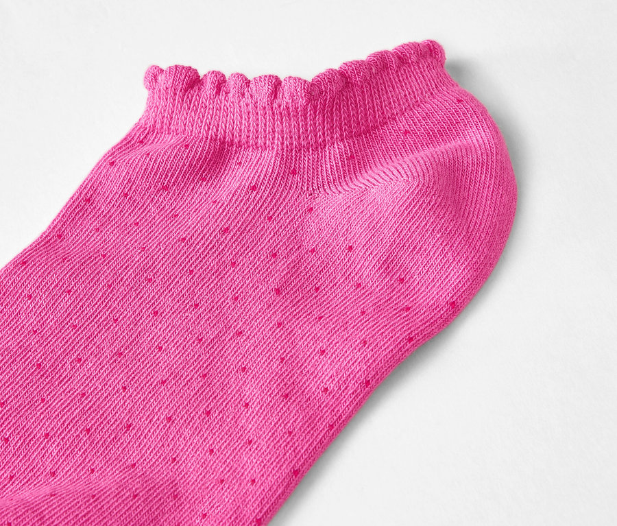 Zbliżenie różowej skarpetki typu stopka z falbanką i kropkami na białym tle.