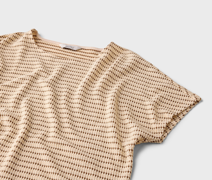 Zbliżenie beżowej bluzki z krótkim rękawem i brązowym wzorem w kropki na szarym tle.