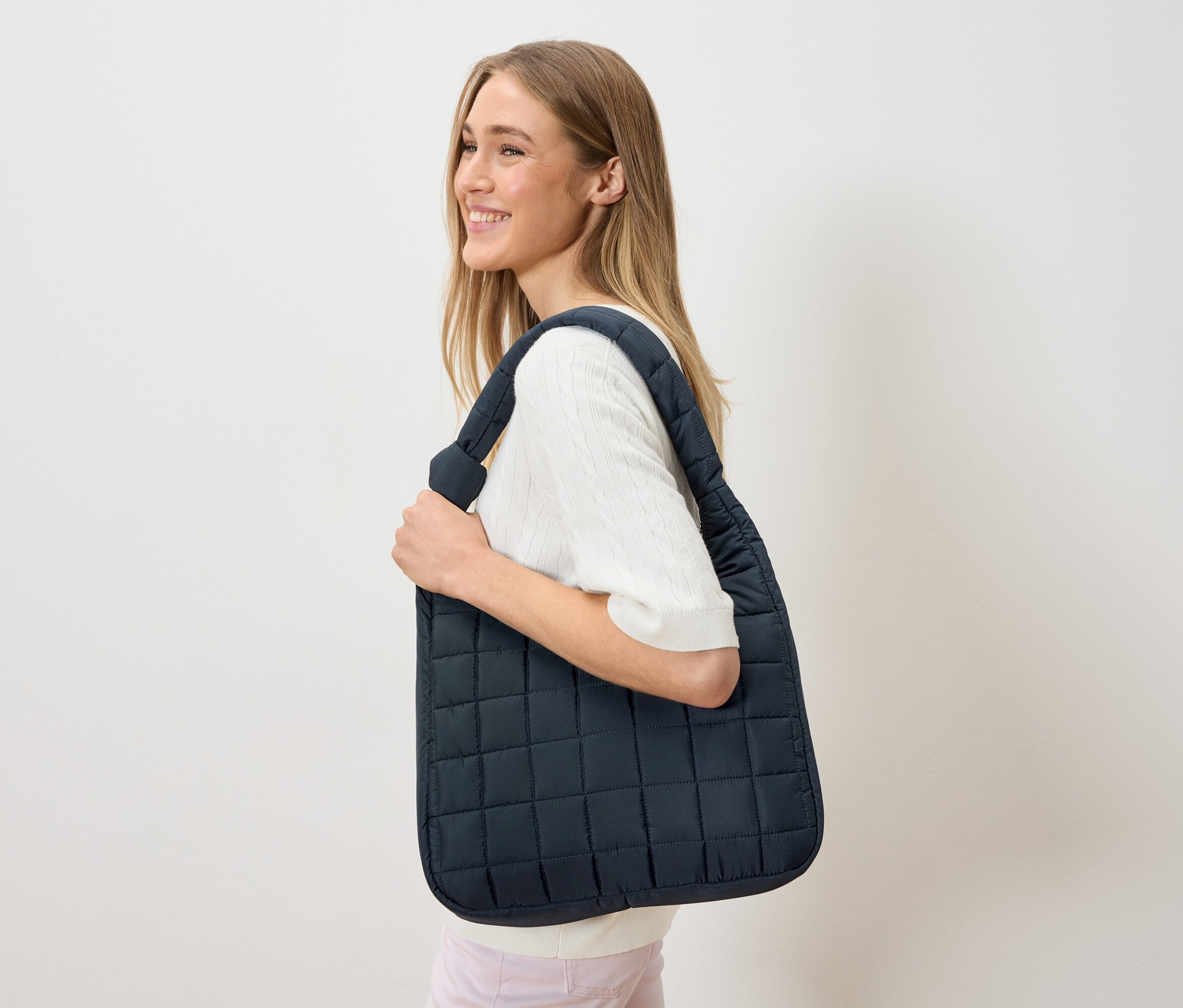 Kobieta nosi na ramieniu granatową, pikowaną torbę.