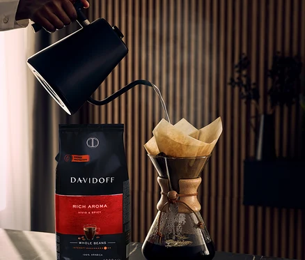 Ręka nalewa wodę z czajnika do filtra do kawy obok paczki DAVIDOFF CAFÉ Rich Aroma.