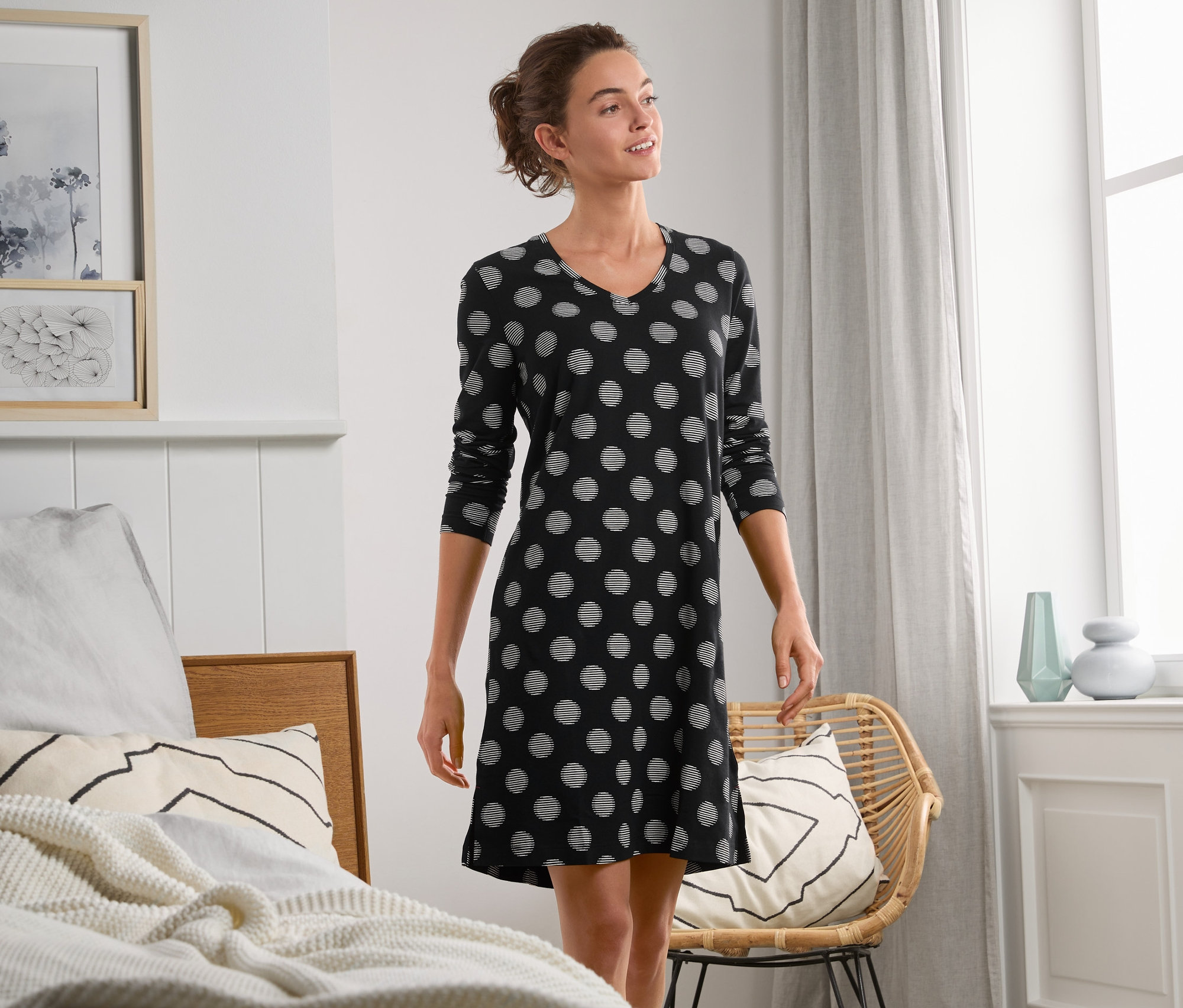 Kobieta w koszuli nocnej w czarne kropki stoi w sypialni.