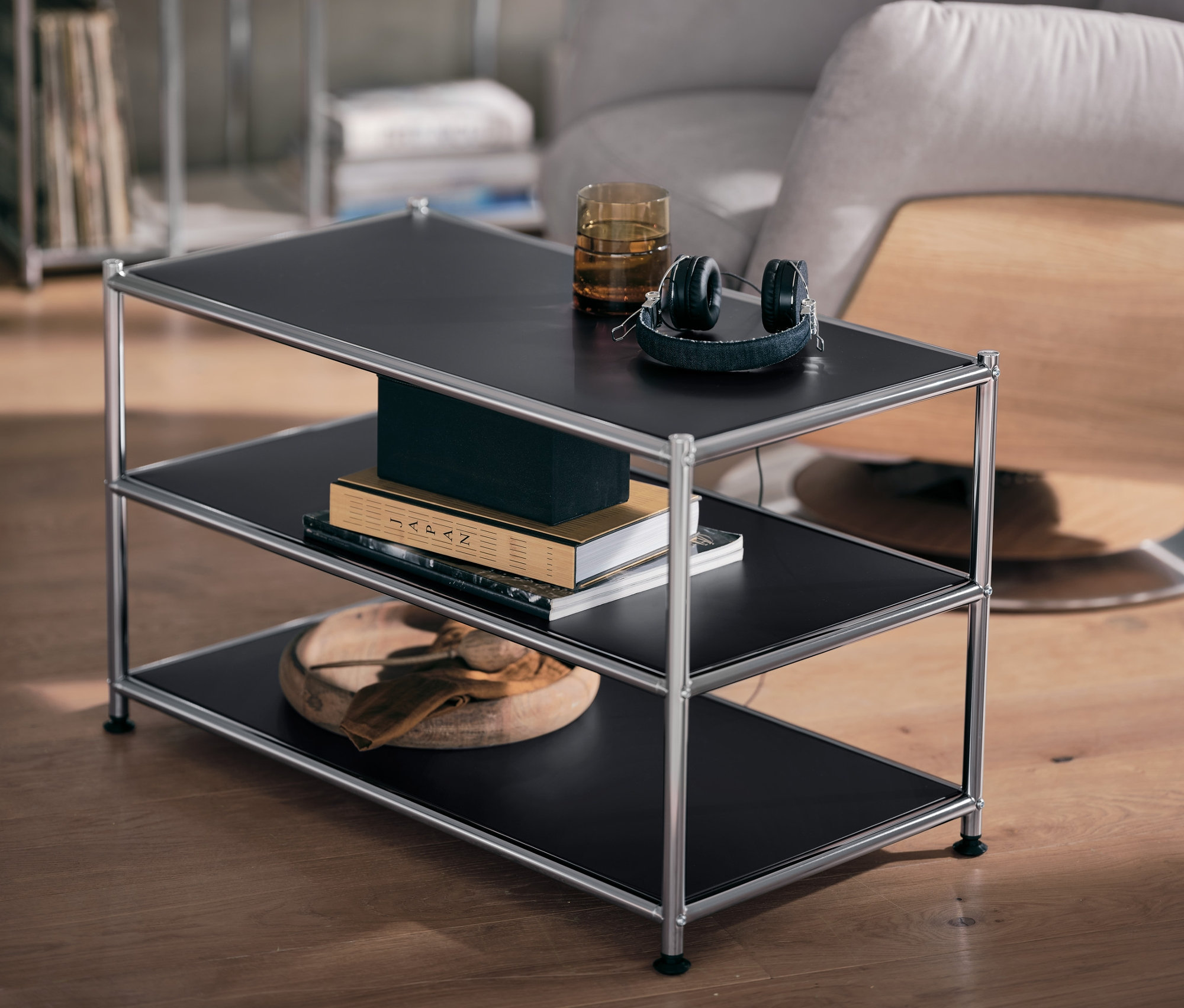 Czarny metalowy stolik »CN3« ze szklanką i słuchawkami na górnej półce.