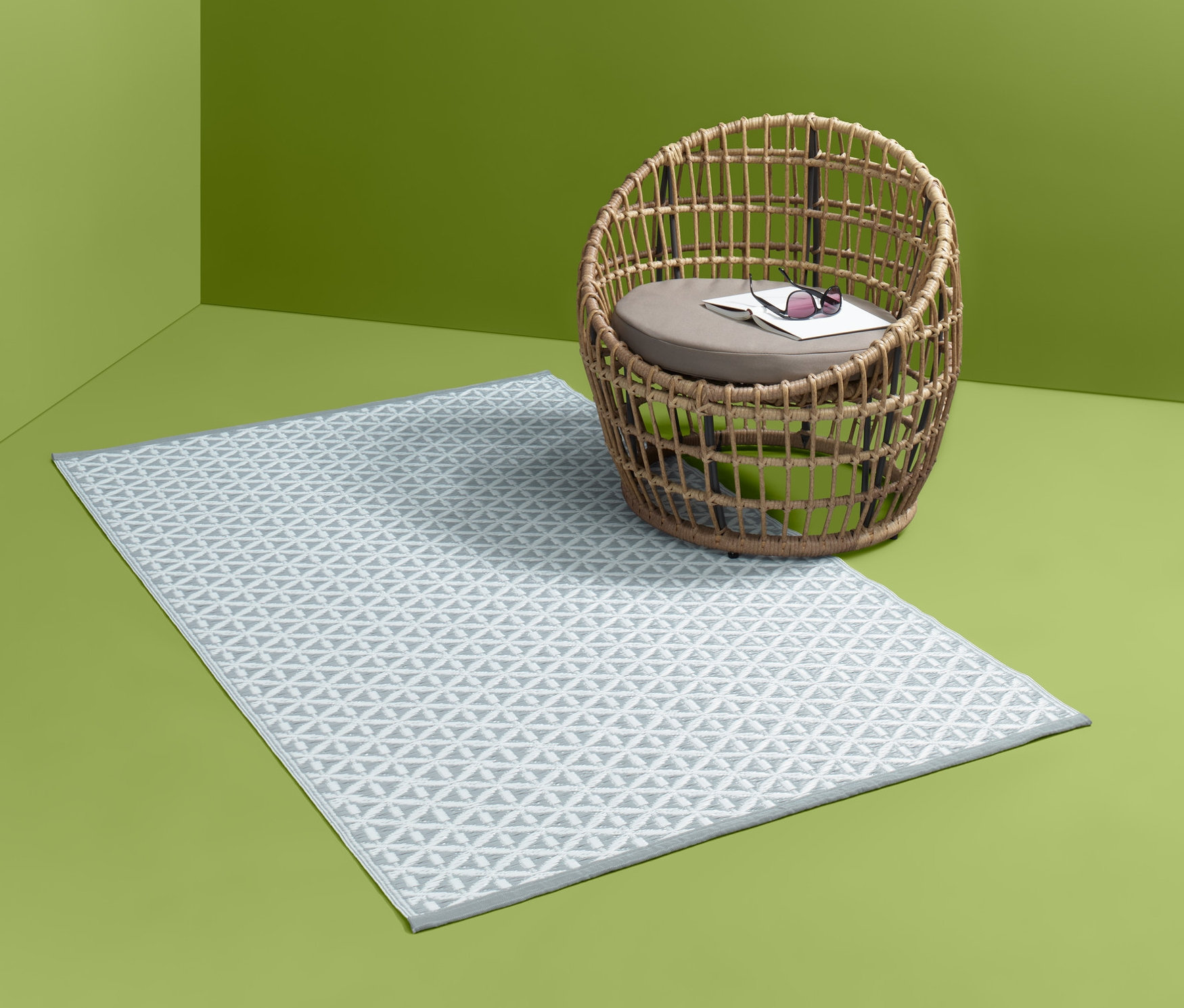 Wzorzysty dywan ogrodowy leży obok wiklinowego krzesła w zielonym rogu pokoju.