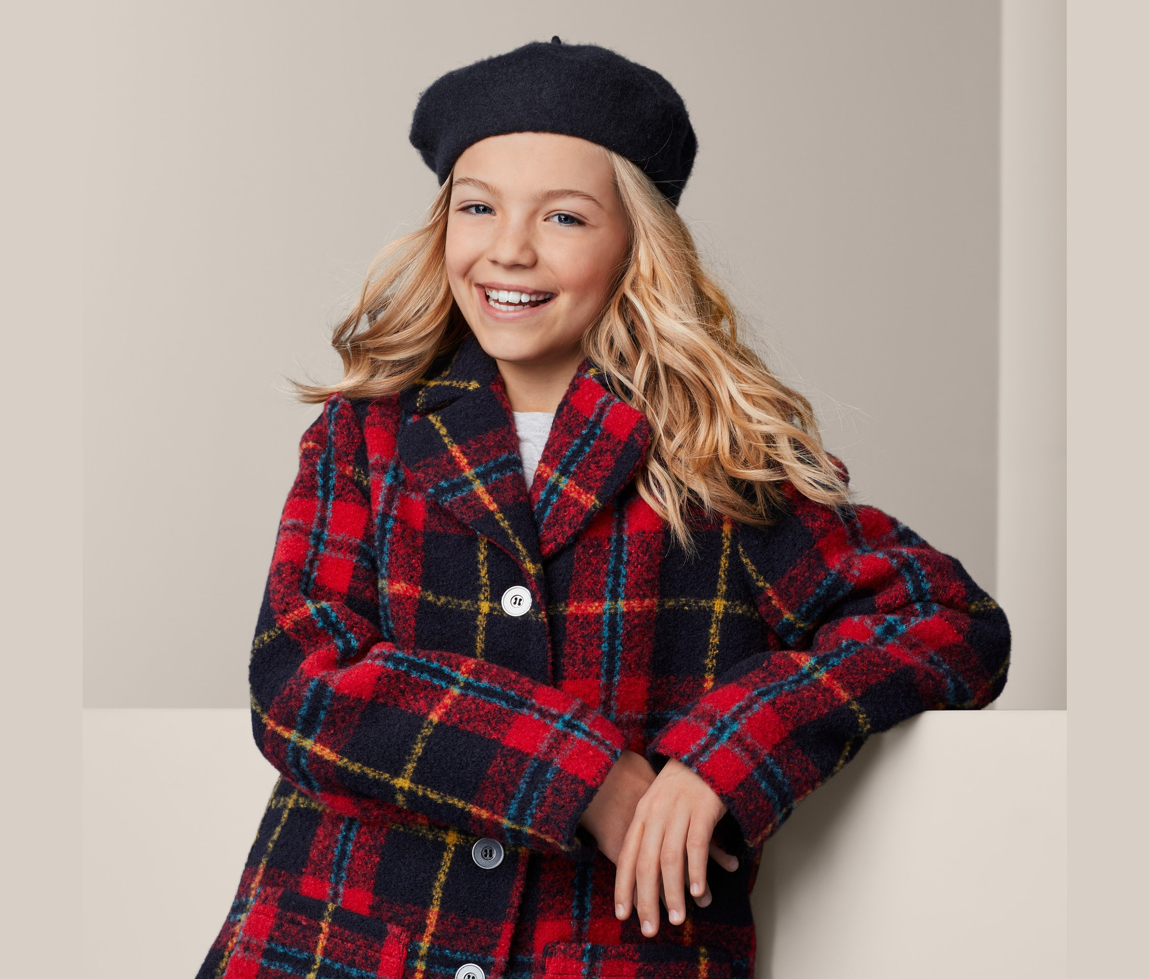 Uśmiechnięta dziewczyna w kraciastej kurtce i berecie.