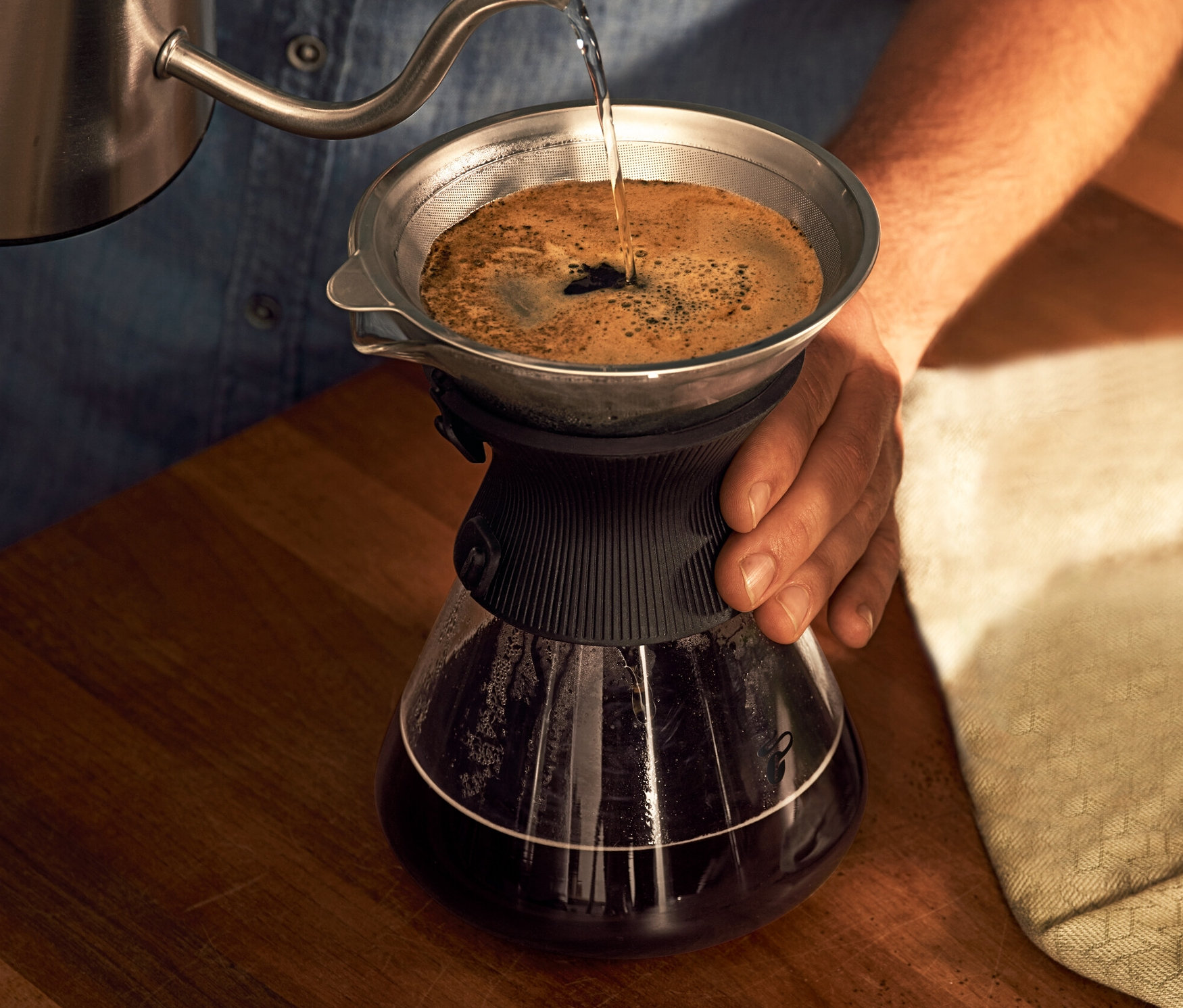 Mężczyzna nalewa wodę do szklanej karafki BEEM Pour Over 0,75 l z filtrem do kawy.