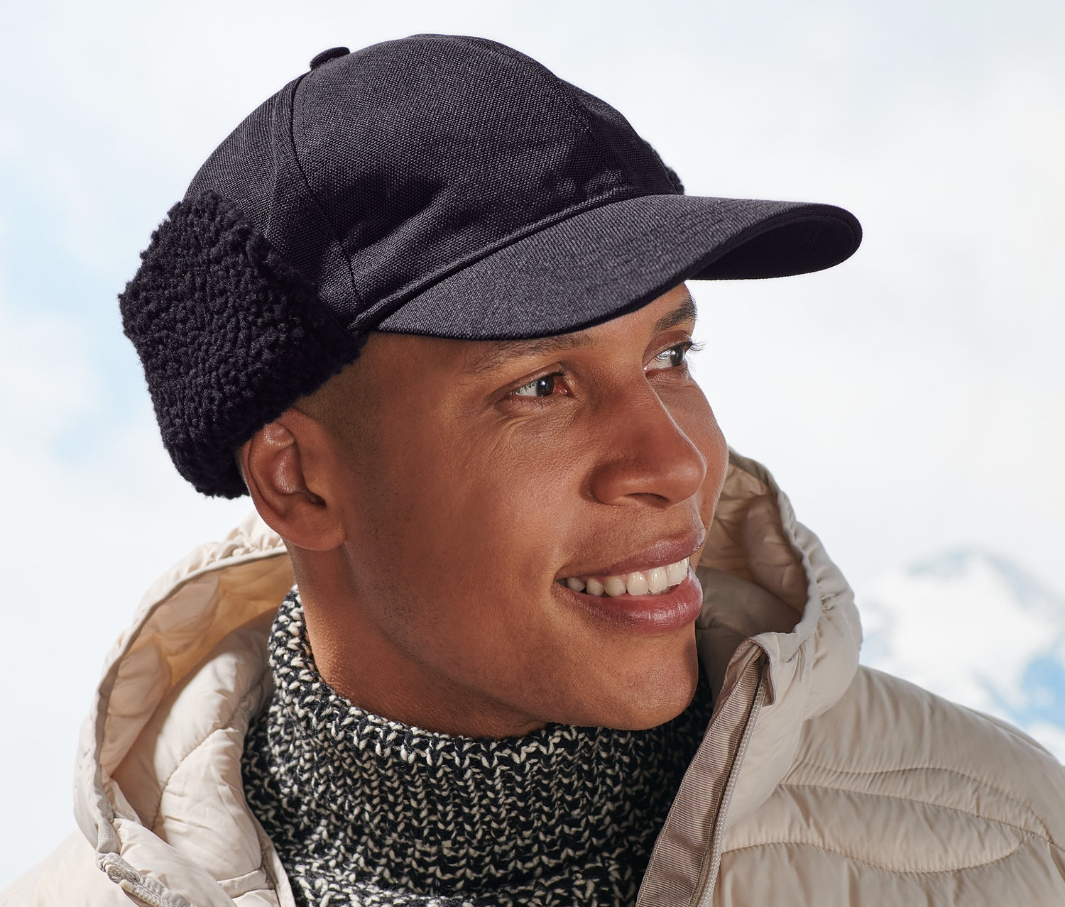 Uśmiechnięty mężczyzna w beżowej kurtce i czapce funkcyjnej.