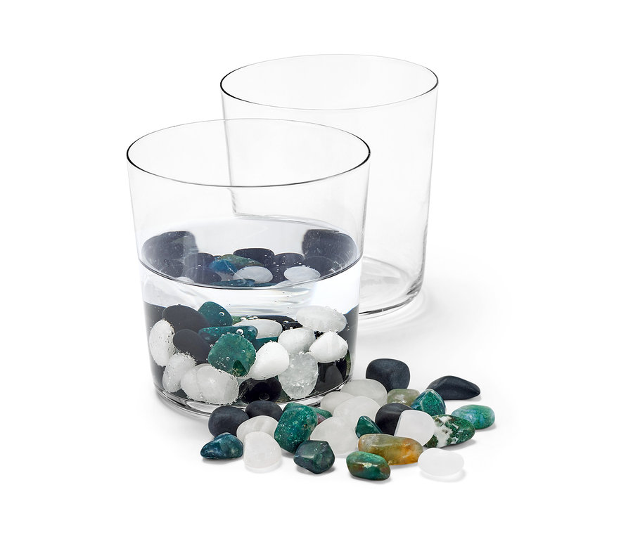 Dwie szklanki, jedna z wodą i kamieniami do wody, druga pusta.