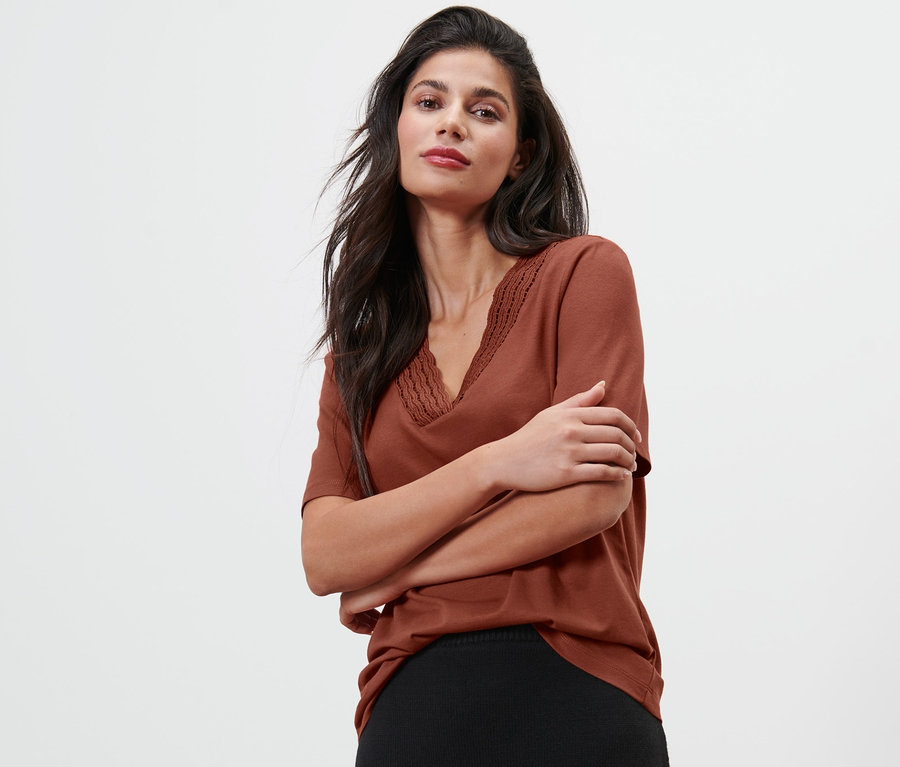 Kobieta pozuje w czerwonobrązowej bluzce.