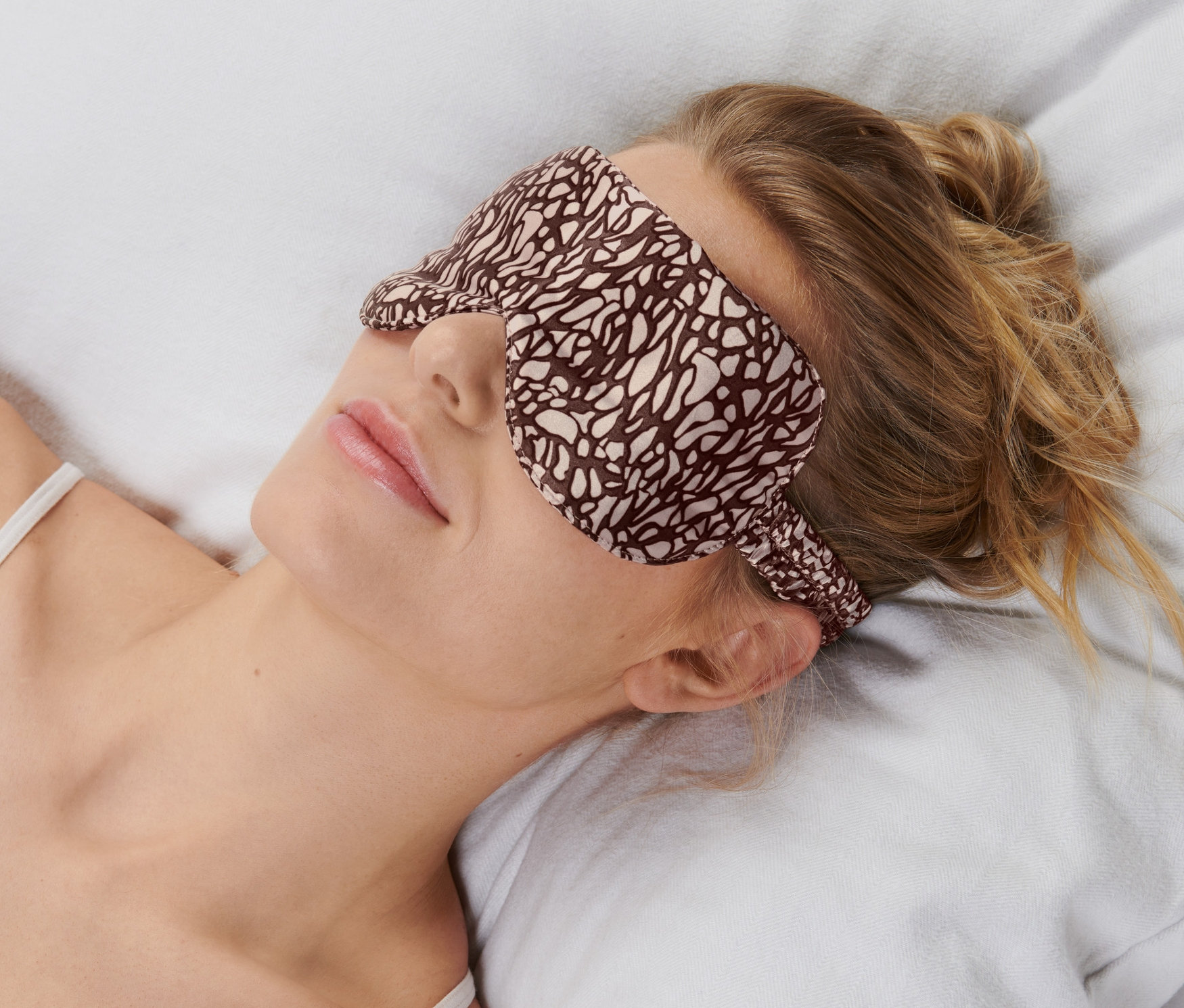 Kobieta leży na poduszce w masce do spania.