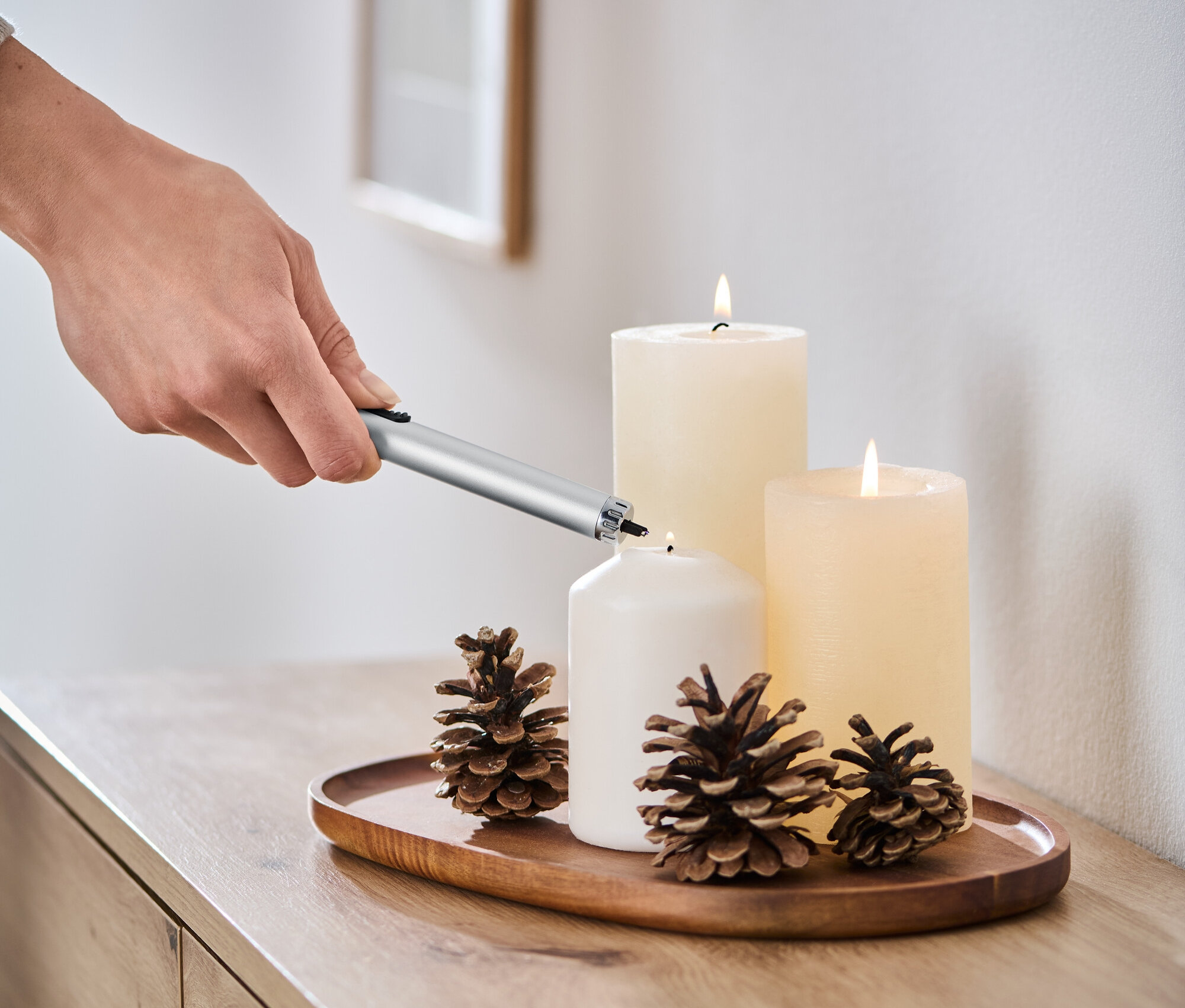 Ręka zapala białą świecę za pomocą zapalniczki plazmowej.