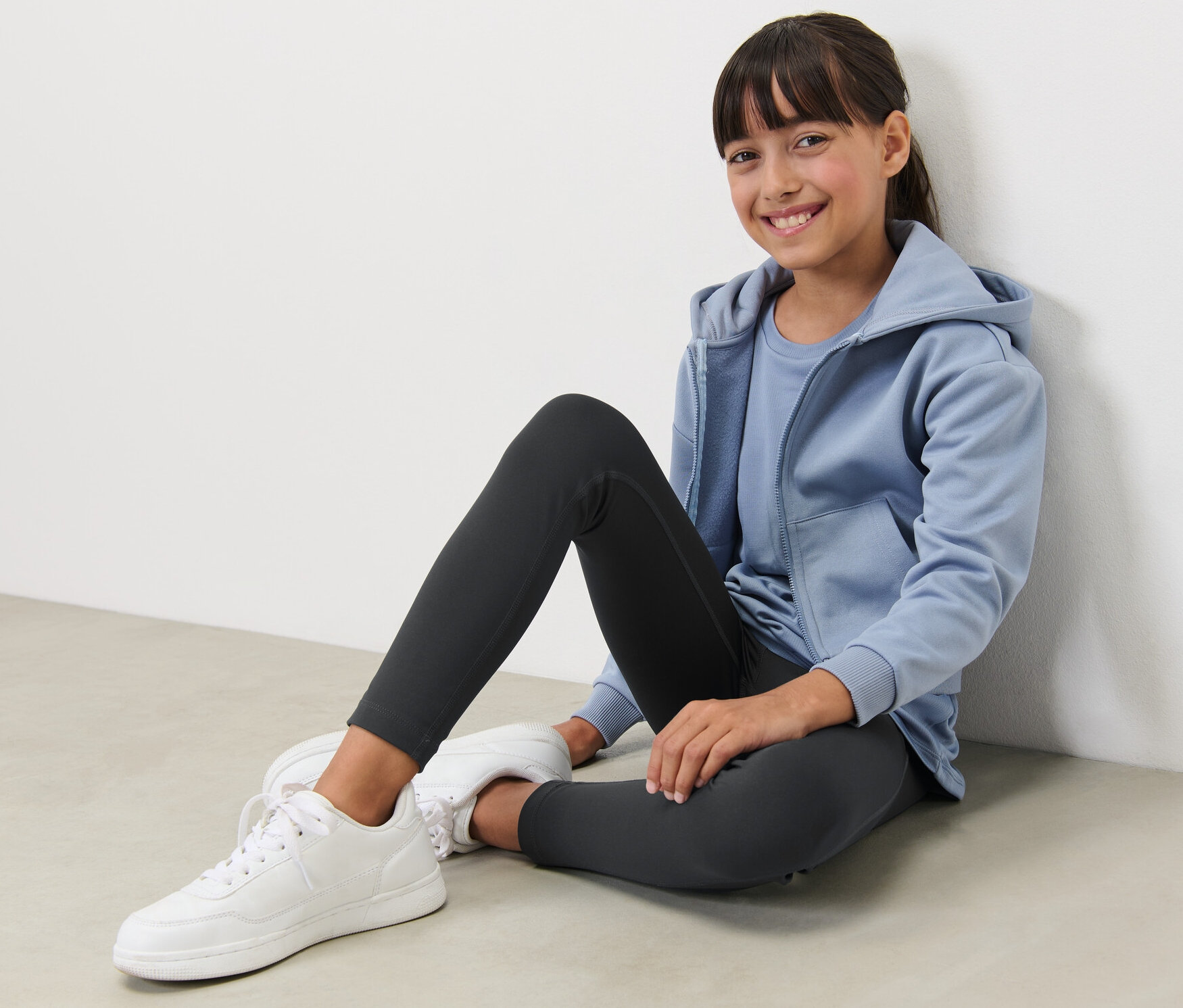 Uśmiechnięta dziewczyna siedzi na podłodze i ma na sobie czarne legginsy sportowe.