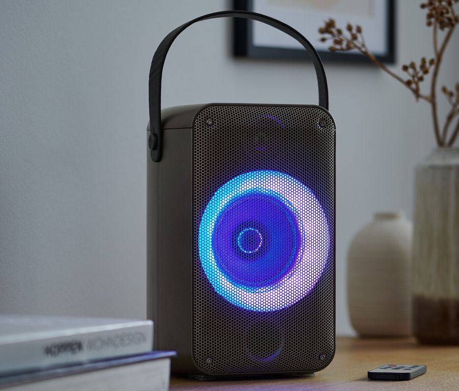 Głośnik Bluetooth® z efektami świetlnymi stoi na stole obok książek i pilota.