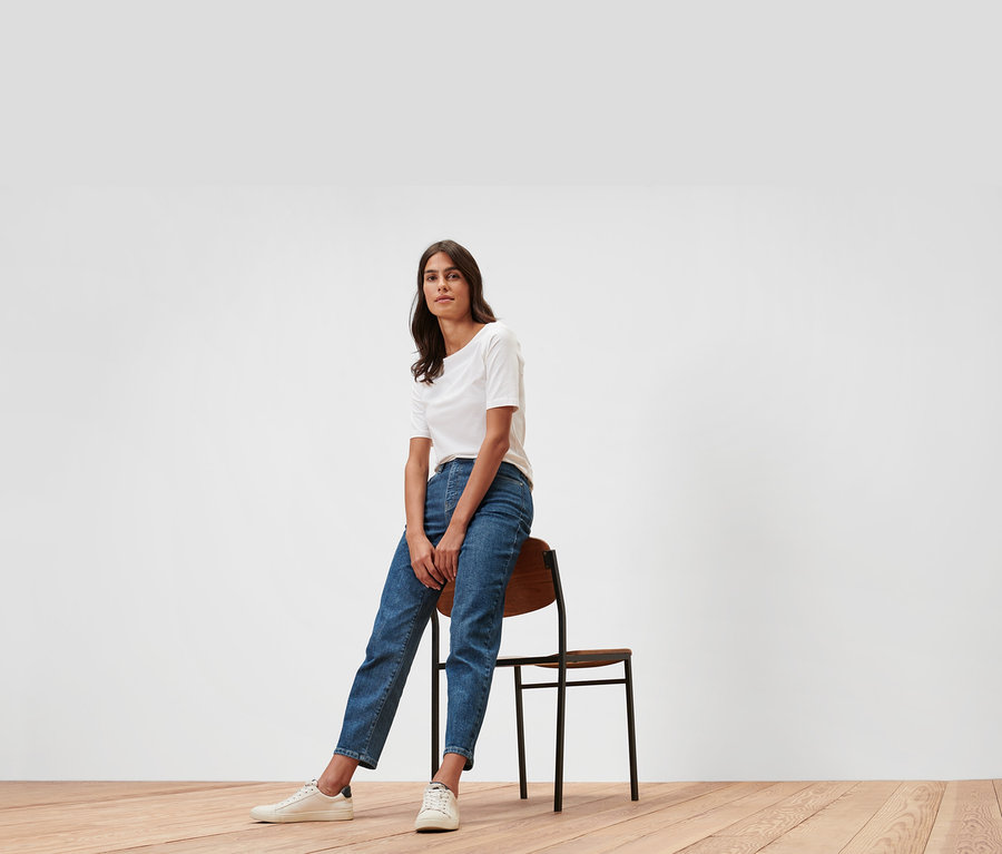 Kobieta siedzi na krześle w dżinsach typu Mom Jeans – fason „Nyla” i białym T-shircie.