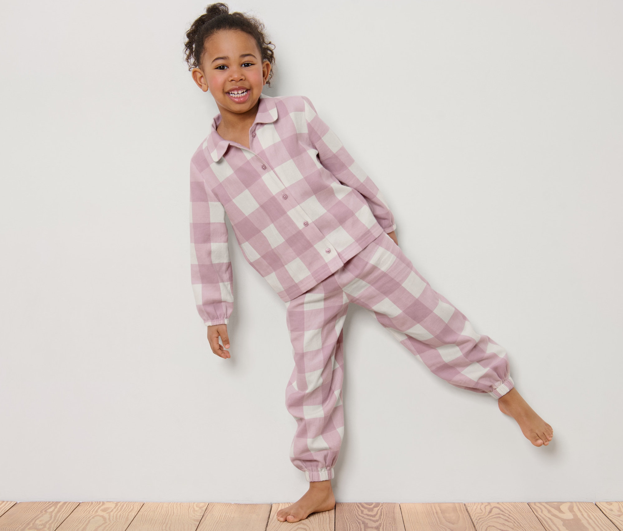 Uśmiechnięta dziewczynka pozuje w flanelowej piżamie w kratę.
