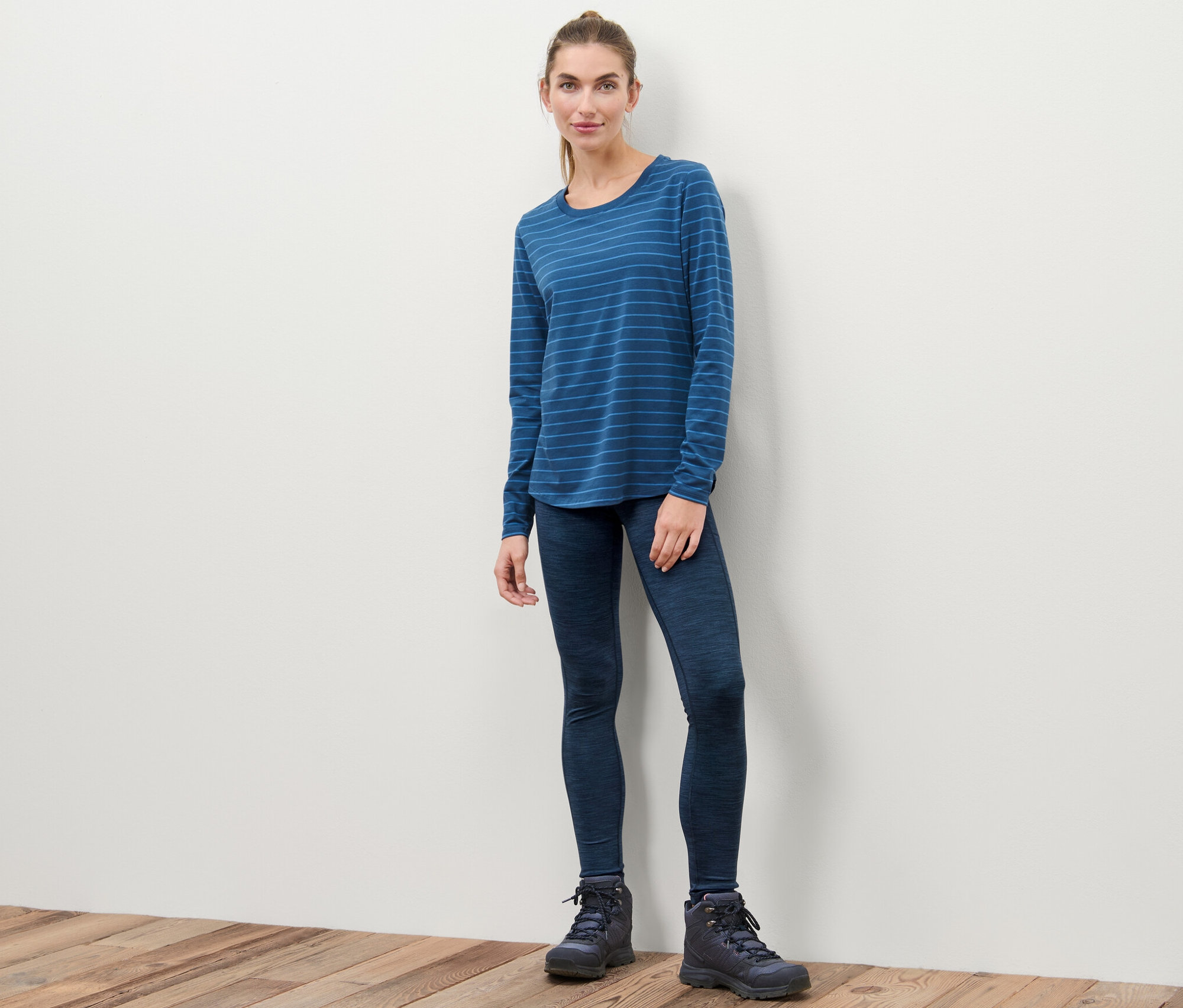 Kobieta stoi w legginsach sportowych, bluzce z długim rękawem w niebieskie paski i butach.