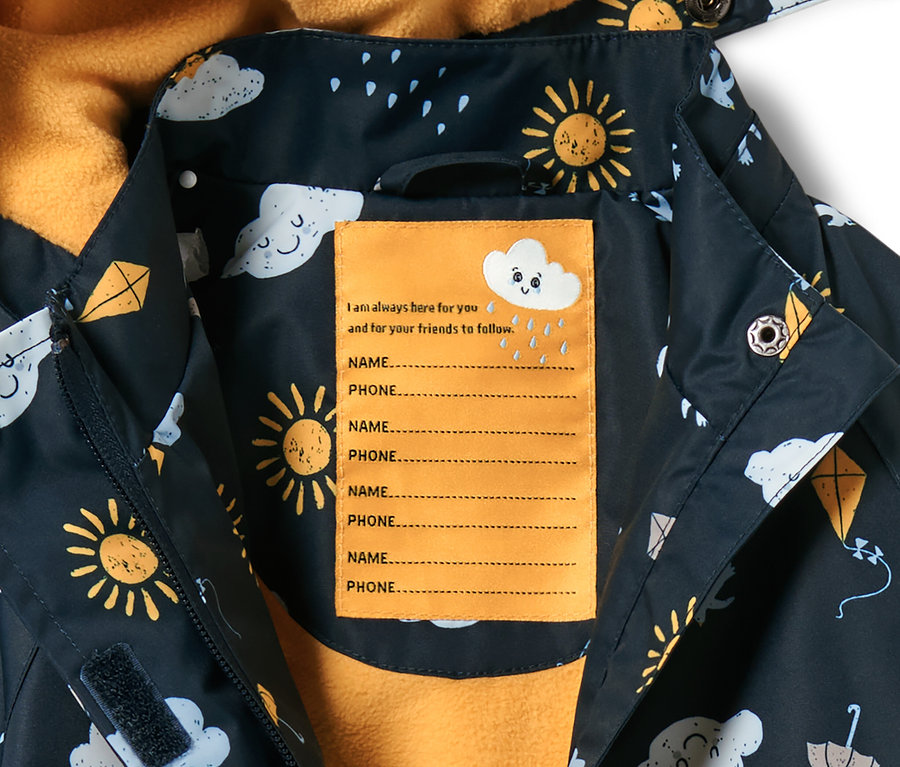 Zbliżenie na granatową, dziecięcą termiczną kurtkę przeciwdeszczową z nadrukiem słońca, chmur i latawców. Wewnątrz znajduje się żółta etykieta na imię i nazwisko oraz numer telefonu.