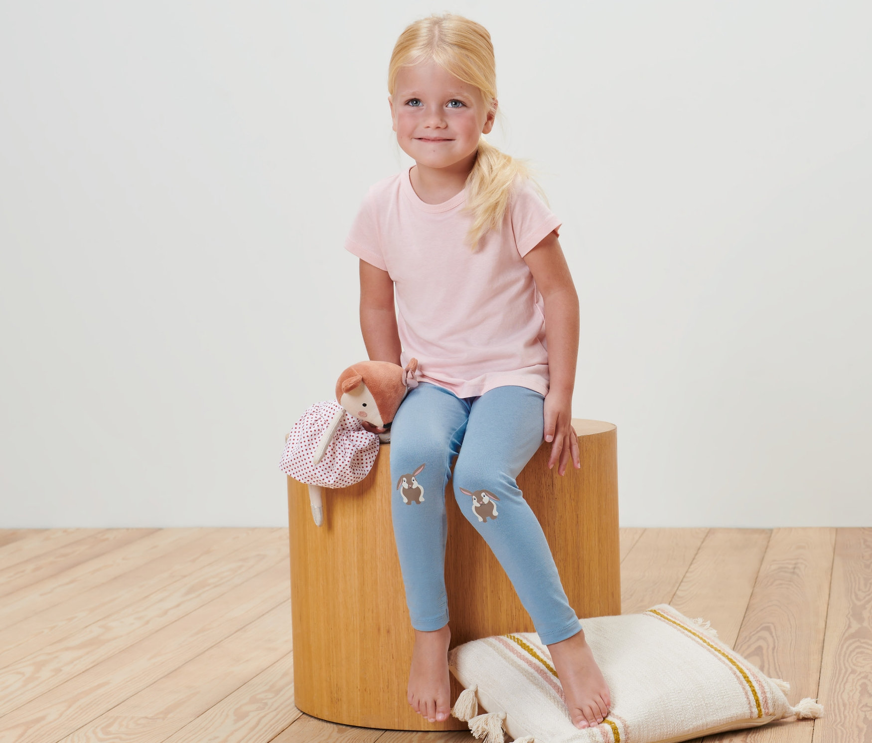 Dziewczynka siedzi na stołku, ubrana w legginsy niemowlęce w paski (2 pary).