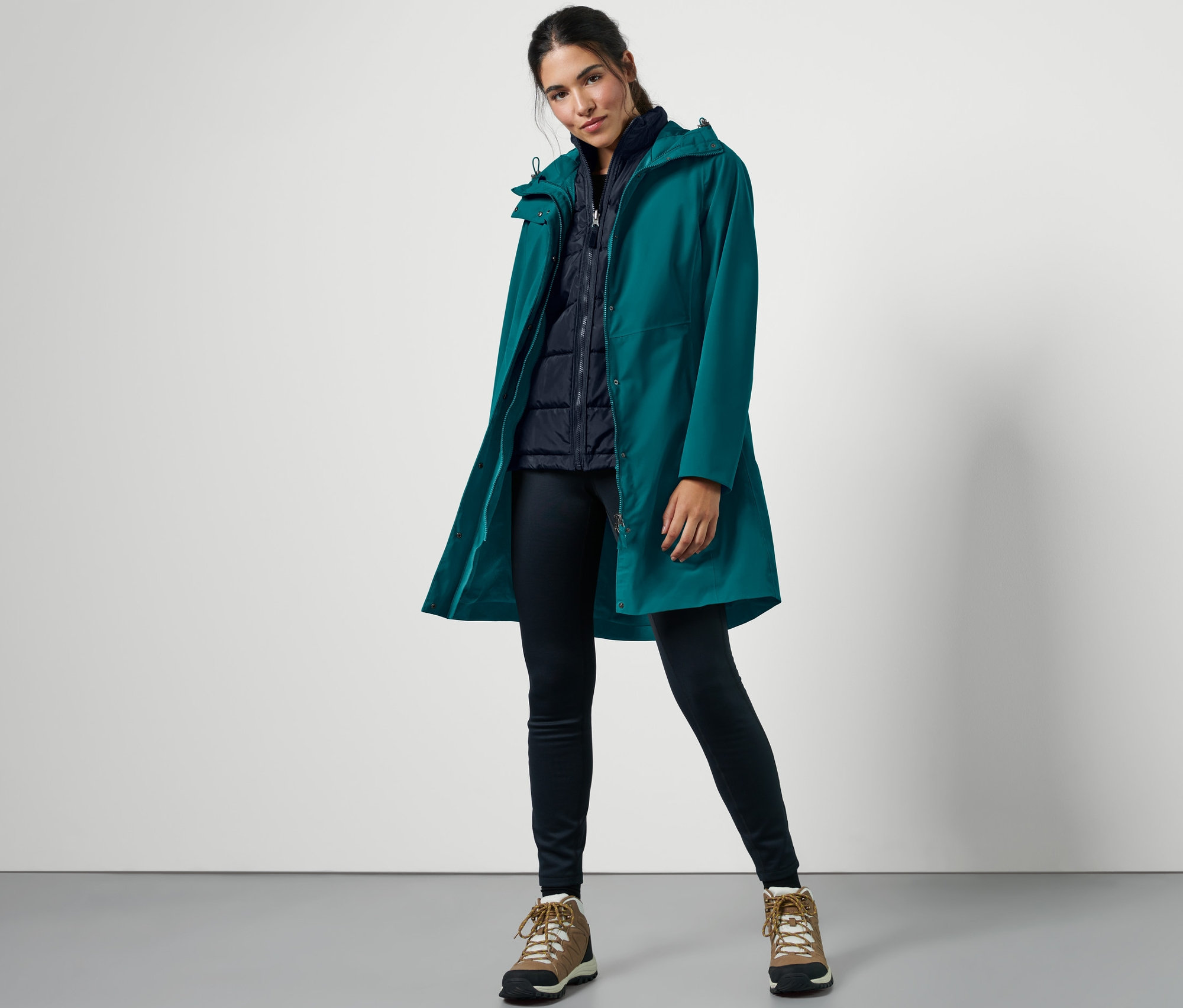 Kobieta pozuje w ciemnoturkusowym płaszczu outdoorowym z kamizelką 3 w 1.