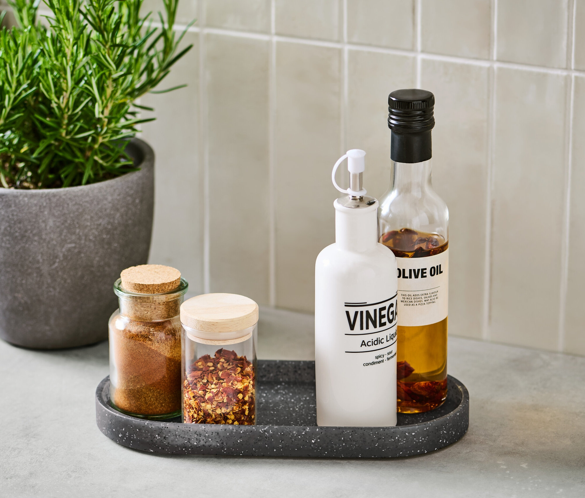 Przyprawy i butelki na tacce z imitacji granitu obok rośliny doniczkowej.
