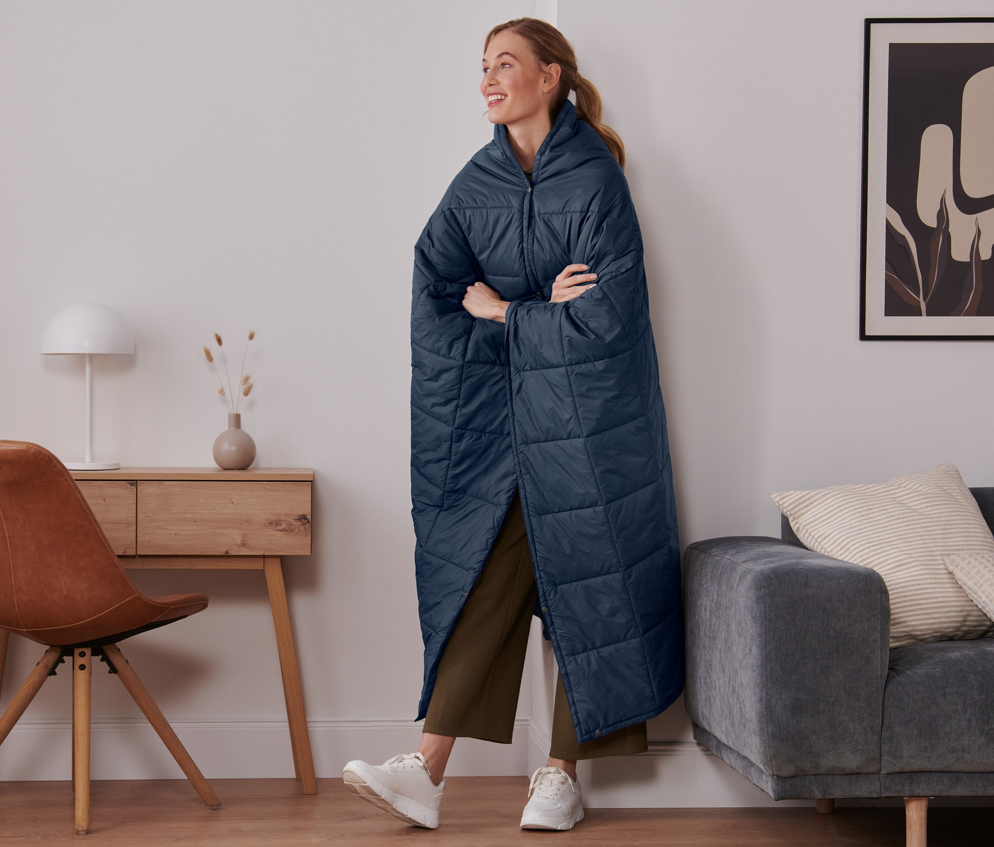 Kobieta stoi w pokoju, ubrana w wyjątkowo lekki koc podróżny.