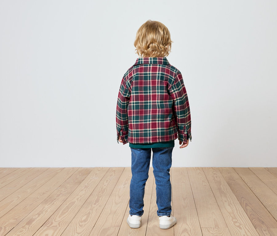 Chłopiec stoi tyłem, ma na sobie koszulę w kratę, dżinsy i trampki.