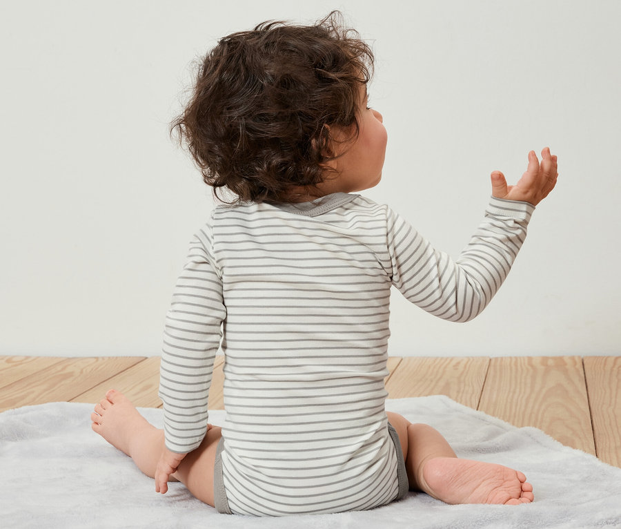 Dziecko siedzi tyłem do kamery na macie i ma na sobie body, 5 par.