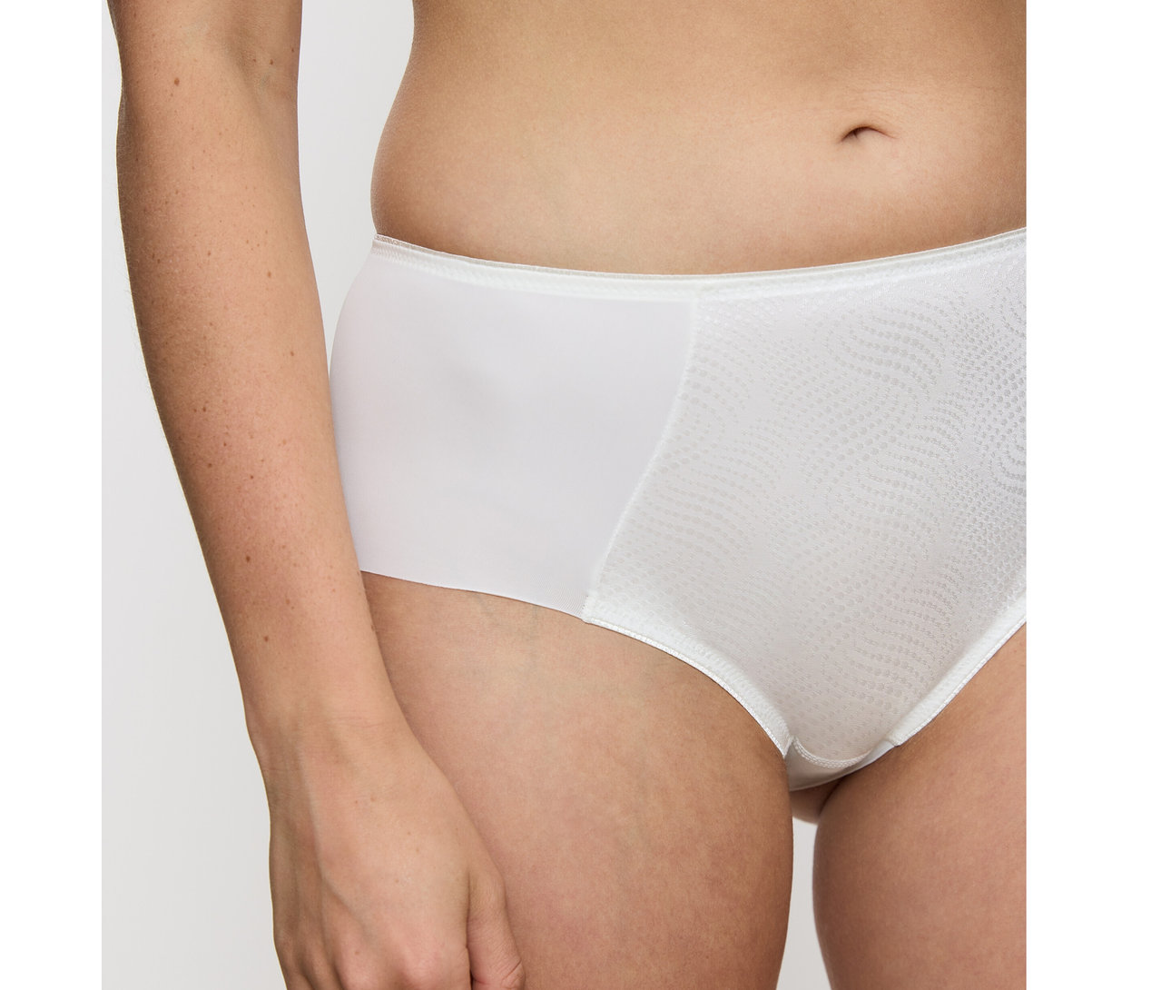 Zbliżenie osoby noszącej waniliowe figi Triumph Essential „Minimizer Hipster X”. Majtki mają teksturowany wzór fal na przodzie.