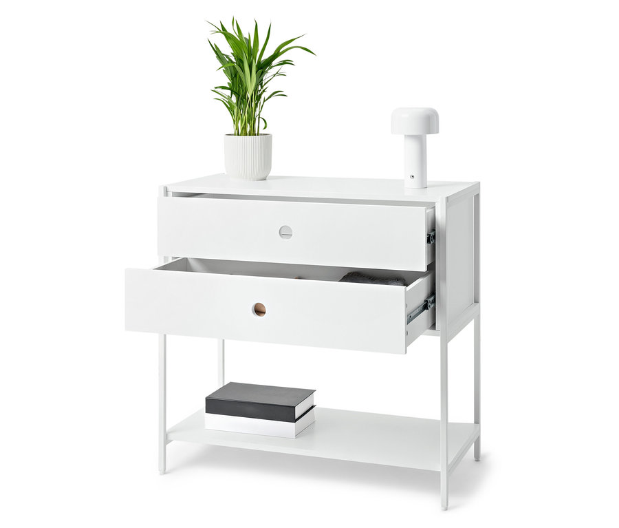 Biały stolik z dwiema szufladami, z których jedna jest otwarta, na którym stoi roślina w doniczce i lampa. Na dolnej półce leżą książki.