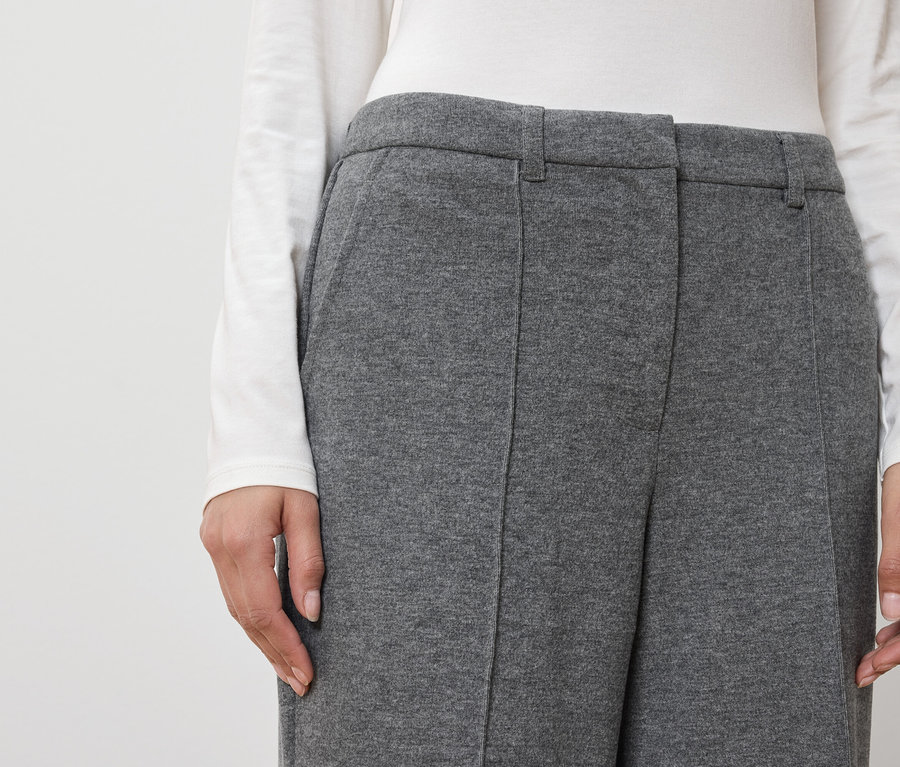 Kobieta ma na sobie szare spodnie i białą bluzkę.