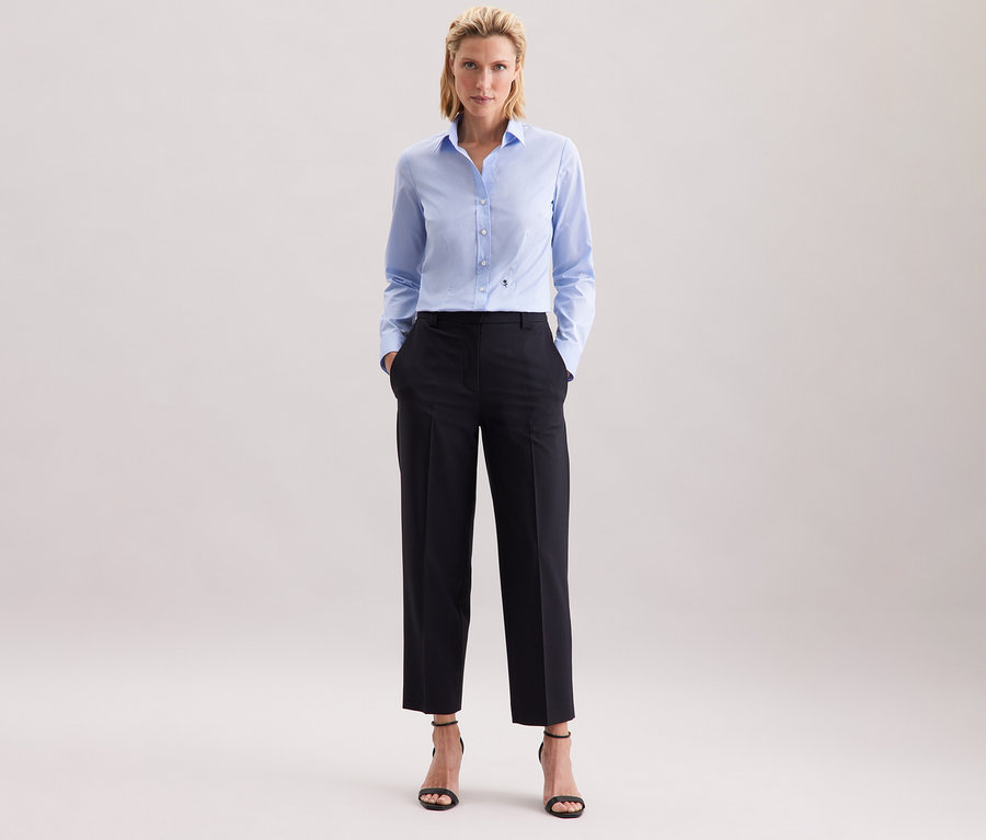 Kobieta w jasnoniebieskiej bluzce Seidensticker Slim Fit non iron i ciemnych spodniach.