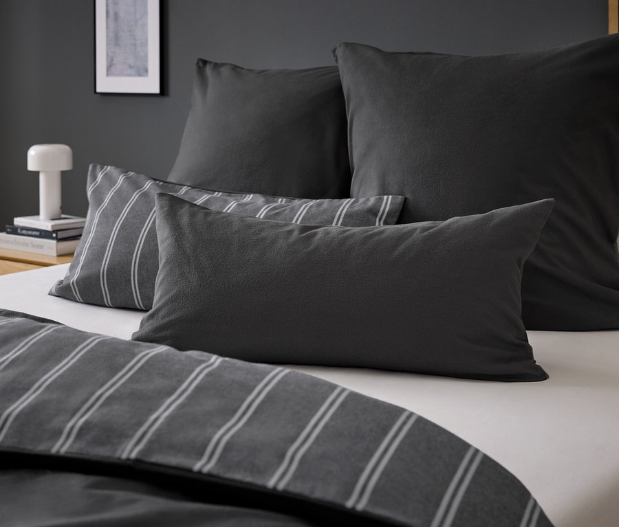 Cztery szare poduszki na łóżku z szarą pościelą w paski.